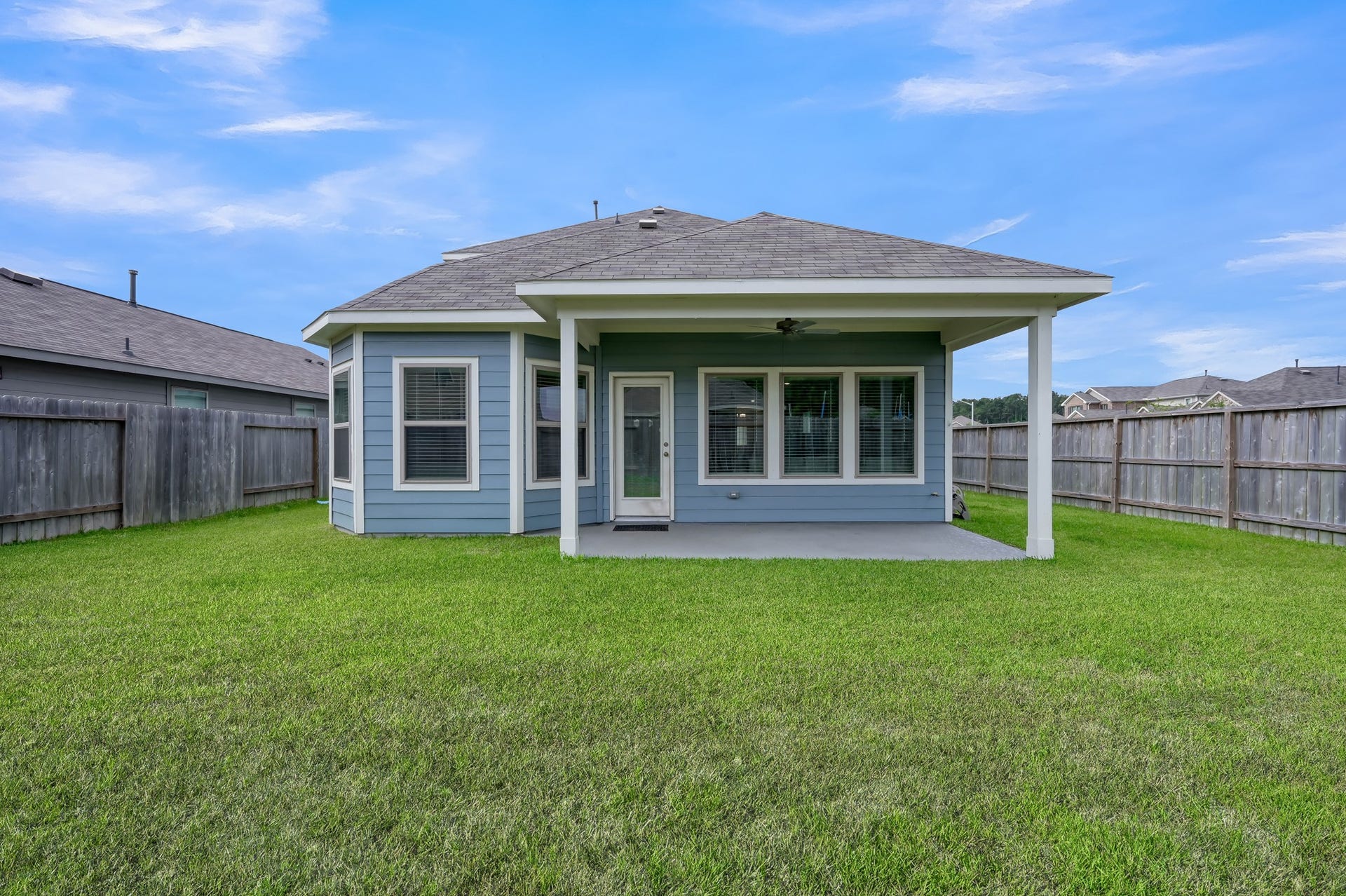 22203 Cardinal Crest Lane, New Caney, TX 77357 This photo shows a charming backyard with a covered patio, perfect for outdoor relaxation or entertaining. The house features a well-maintained lawn and a wooden fence providing privacy.