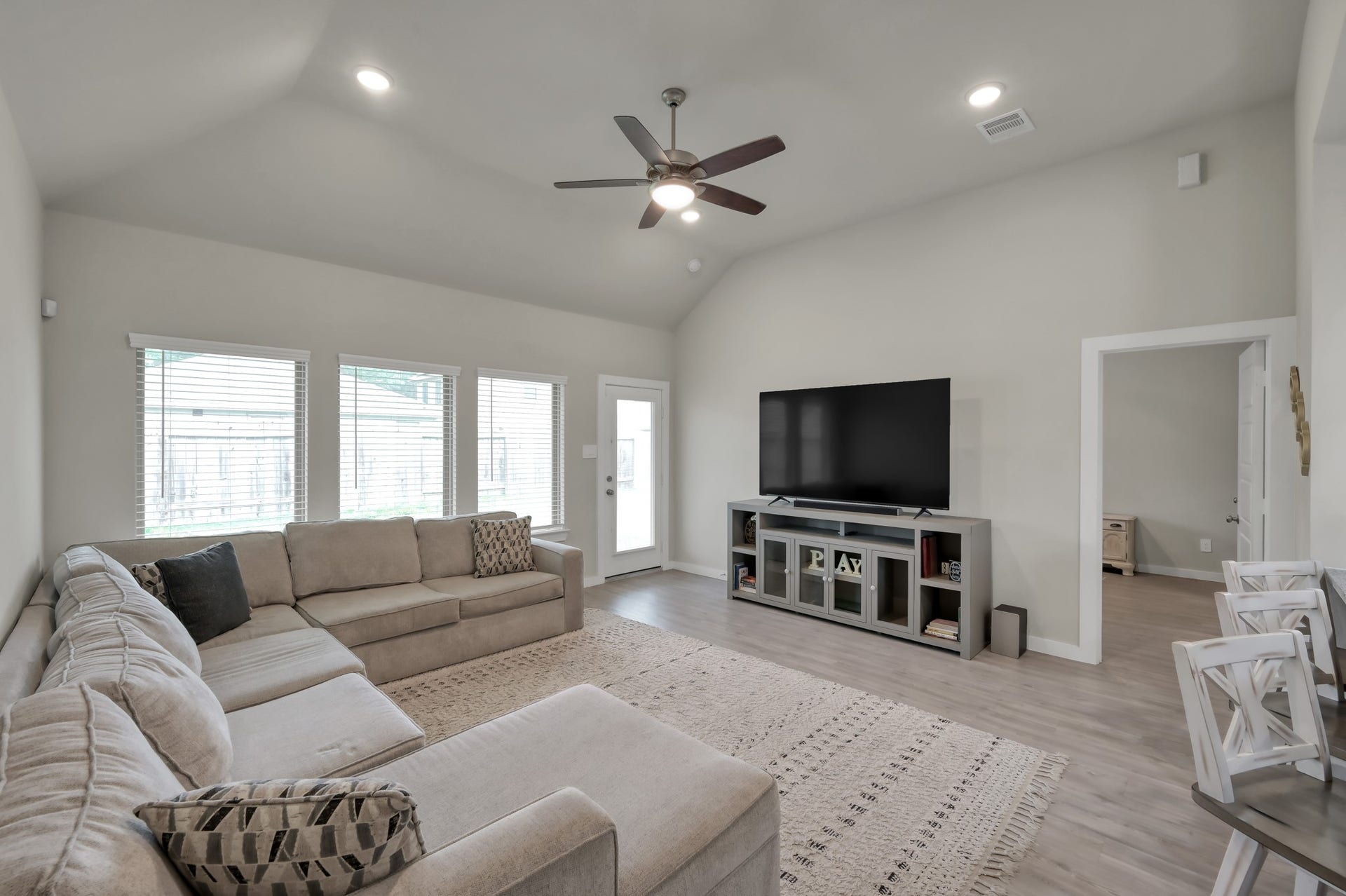 22203 Cardinal Crest Lane, New Caney, TX 77357 Bright and spacious living room with vaulted ceilings, featuring a large sectional sofa, hardwood floors, and ample natural light from multiple windows. A ceiling fan and modern entertainment setup enhance comfort and functionality.