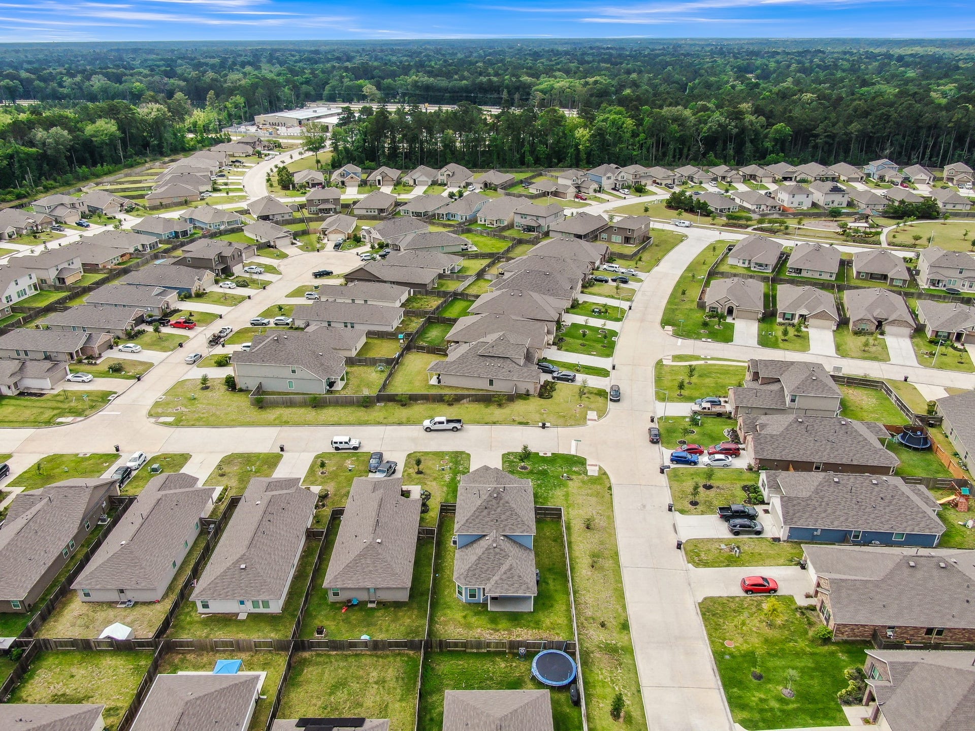 22203 Cardinal Crest Lane, New Caney, TX 77357 This aerial photo showcases a suburban neighborhood with neatly arranged single-family homes, well-maintained lawns, and a backdrop of lush greenery. The streets are wide and offer ample parking, creating a welcoming community atmosphere.