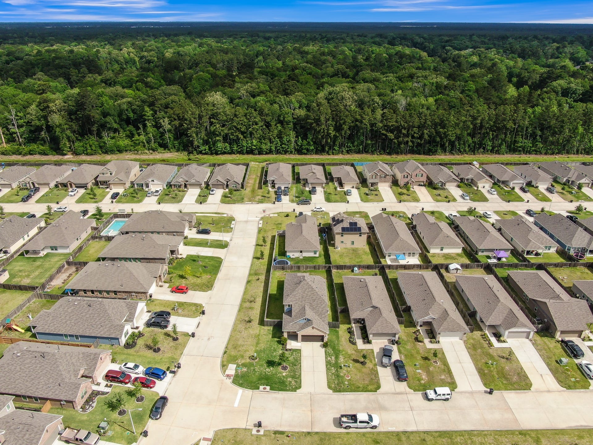 22203 Cardinal Crest Lane, New Caney, TX 77357 This photo showcases a suburban neighborhood with rows of single-family homes, each with driveways and neatly maintained lawns. The area is adjacent to a large, lush forest, providing a scenic backdrop and a sense of privacy.