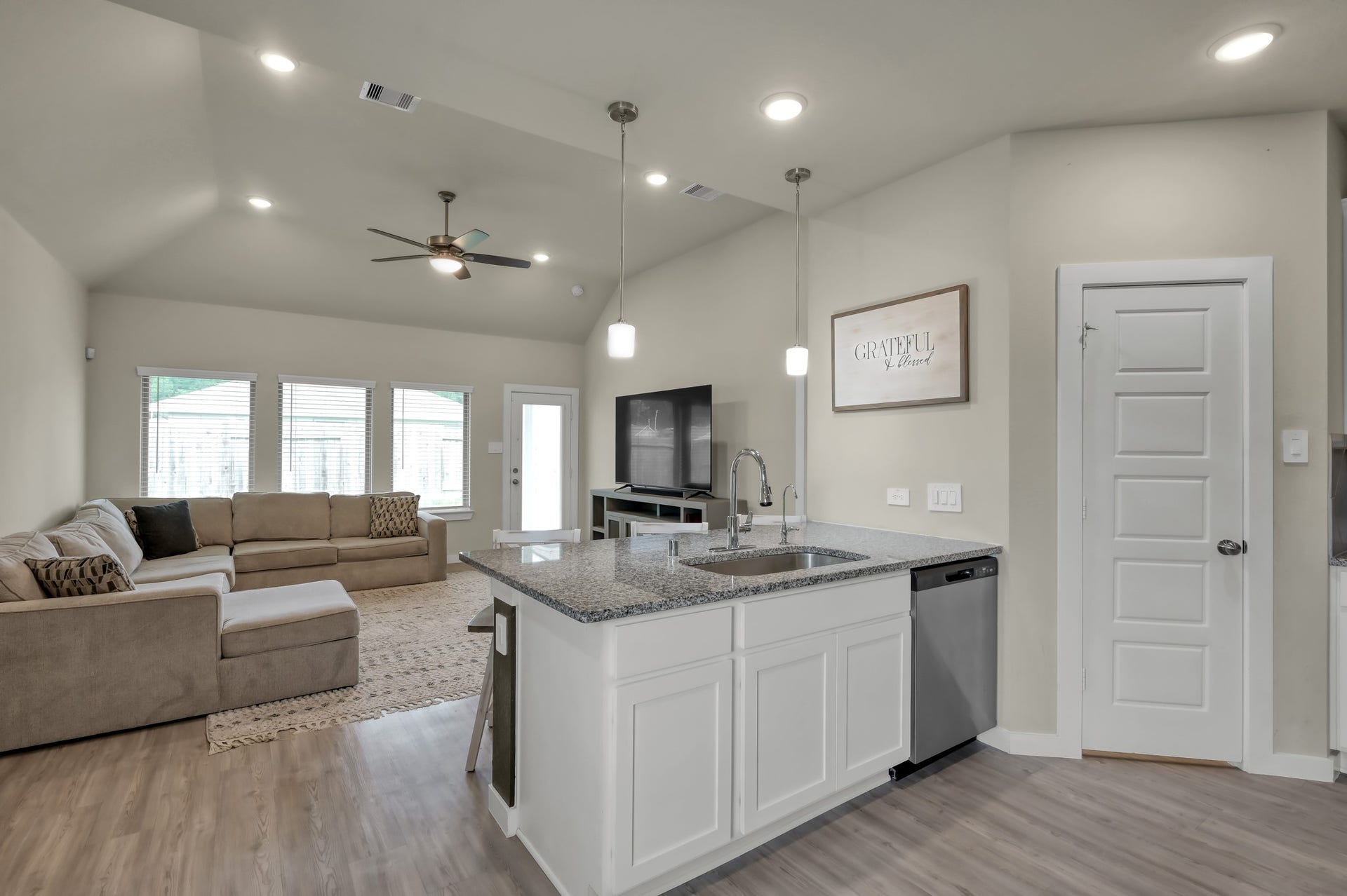 22203 Cardinal Crest Lane, New Caney, TX 77357 This modern, open-concept living space features a cozy sectional sofa, large windows for natural light, and a central kitchen island with granite countertops. The light wood flooring and neutral walls create a warm, inviting atmosphere.