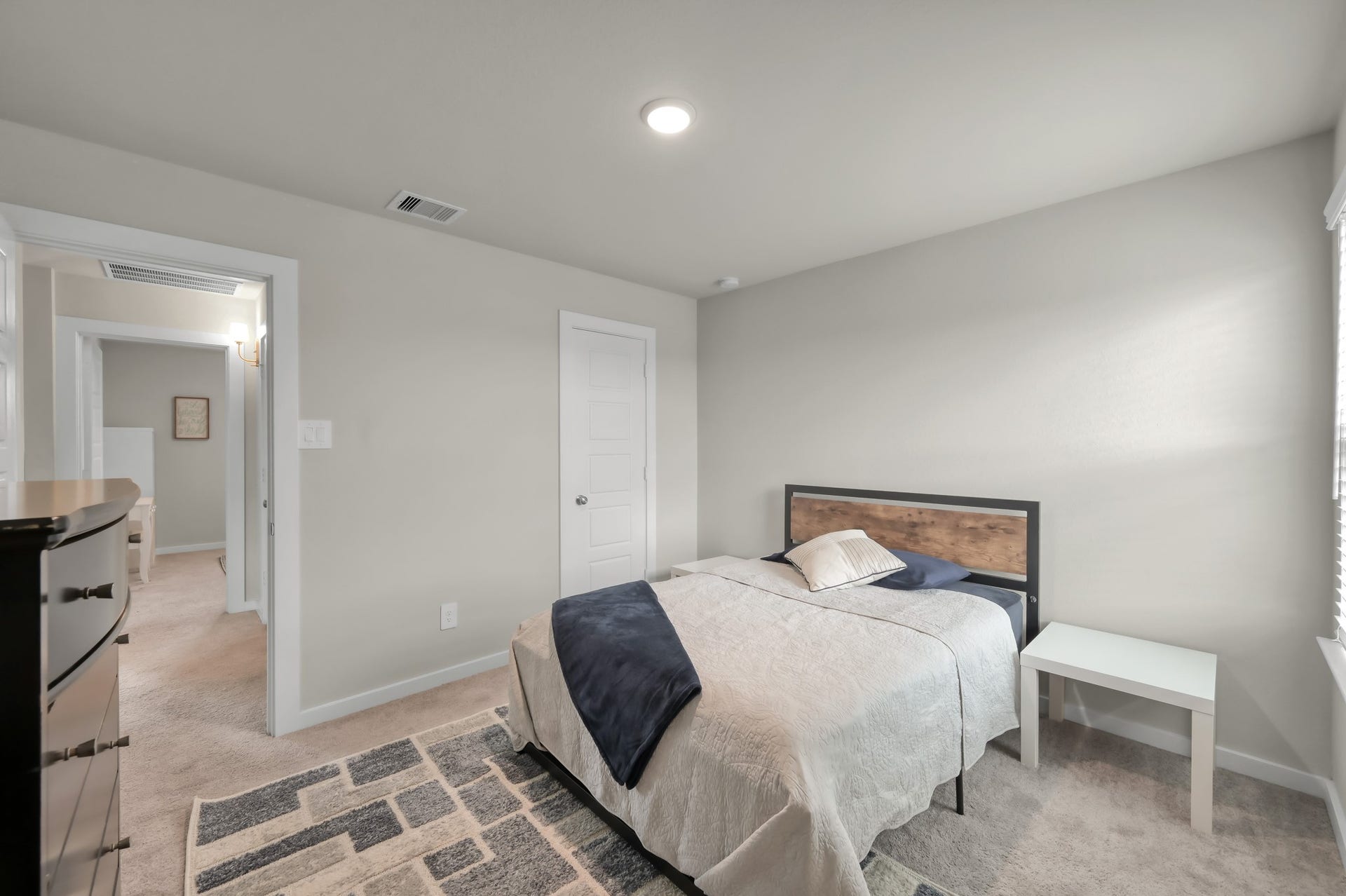 22203 Cardinal Crest Lane, New Caney, TX 77357 A cozy bedroom with neutral tones, featuring a bed with a wooden headboard, a side table, and a dresser. The room has carpeted flooring and is well-lit, providing a warm and inviting atmosphere.