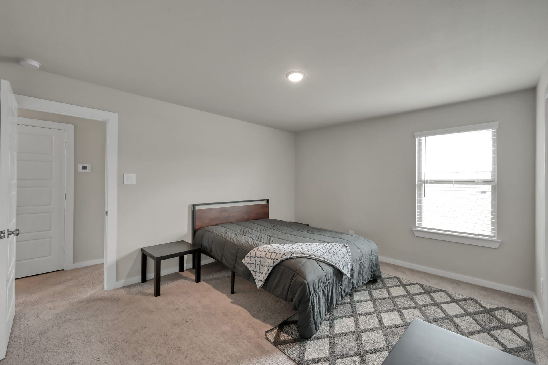 22203 Cardinal Crest Lane, New Caney, TX 77357 This cozy bedroom features neutral walls, a carpeted floor, and ample natural light from a single window. It includes a bed with a simple headboard and a small side table, creating a comfortable, minimalist space.