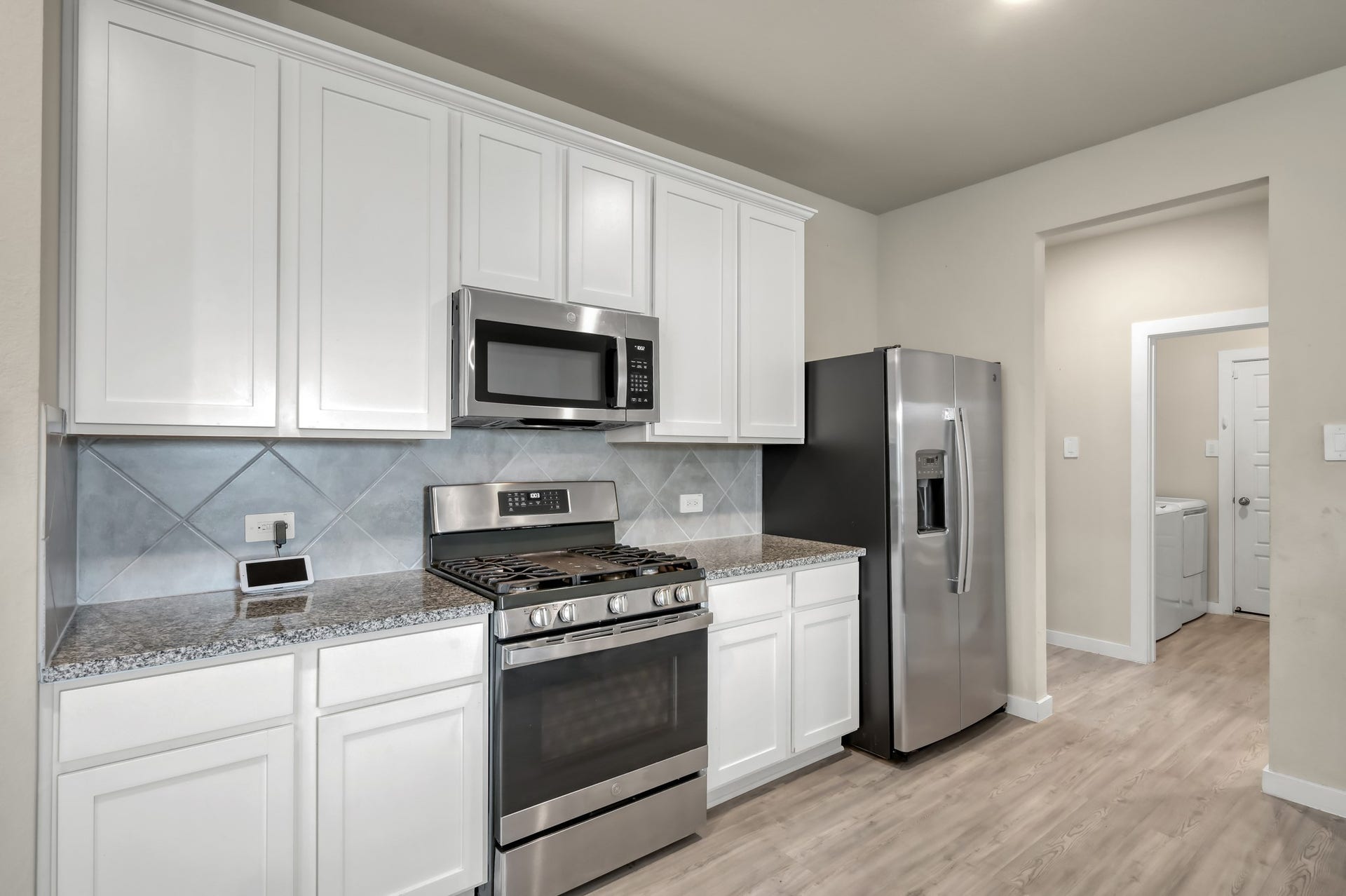 22203 Cardinal Crest Lane, New Caney, TX 77357 This modern kitchen with sleek stainless steel appliances, including a gas stove and refrigerator. Features white cabinetry, granite countertops, and a stylish tile backsplash. Adjacent to a utility room with washer and dryer.