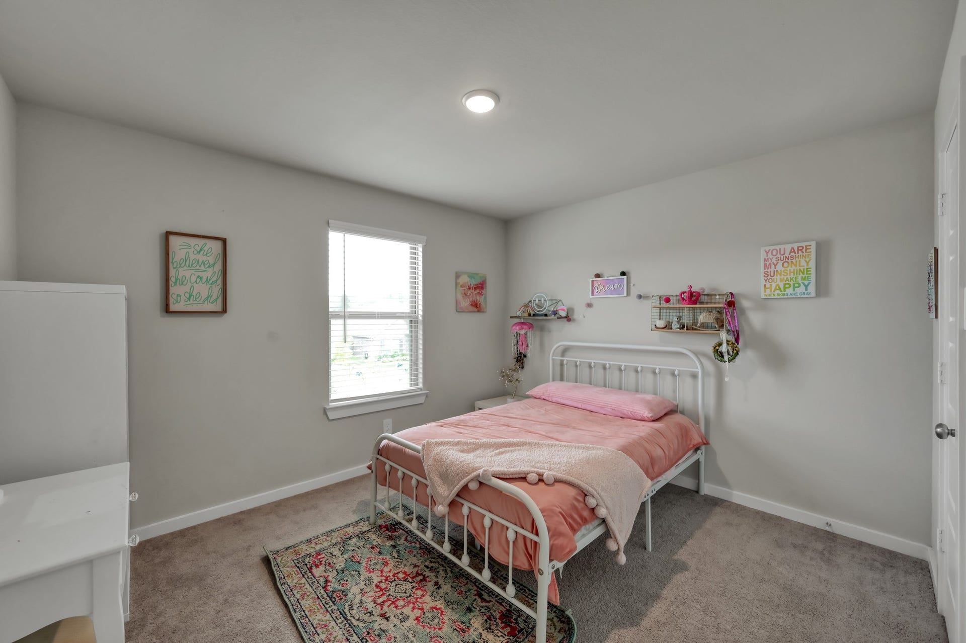 22203 Cardinal Crest Lane, New Caney, TX 77357 This cozy, well-lit bedroom features soft carpeting, a large window for natural light, and a neatly made bed. The walls are adorned with cheerful decorations, creating a welcoming and comfortable space.