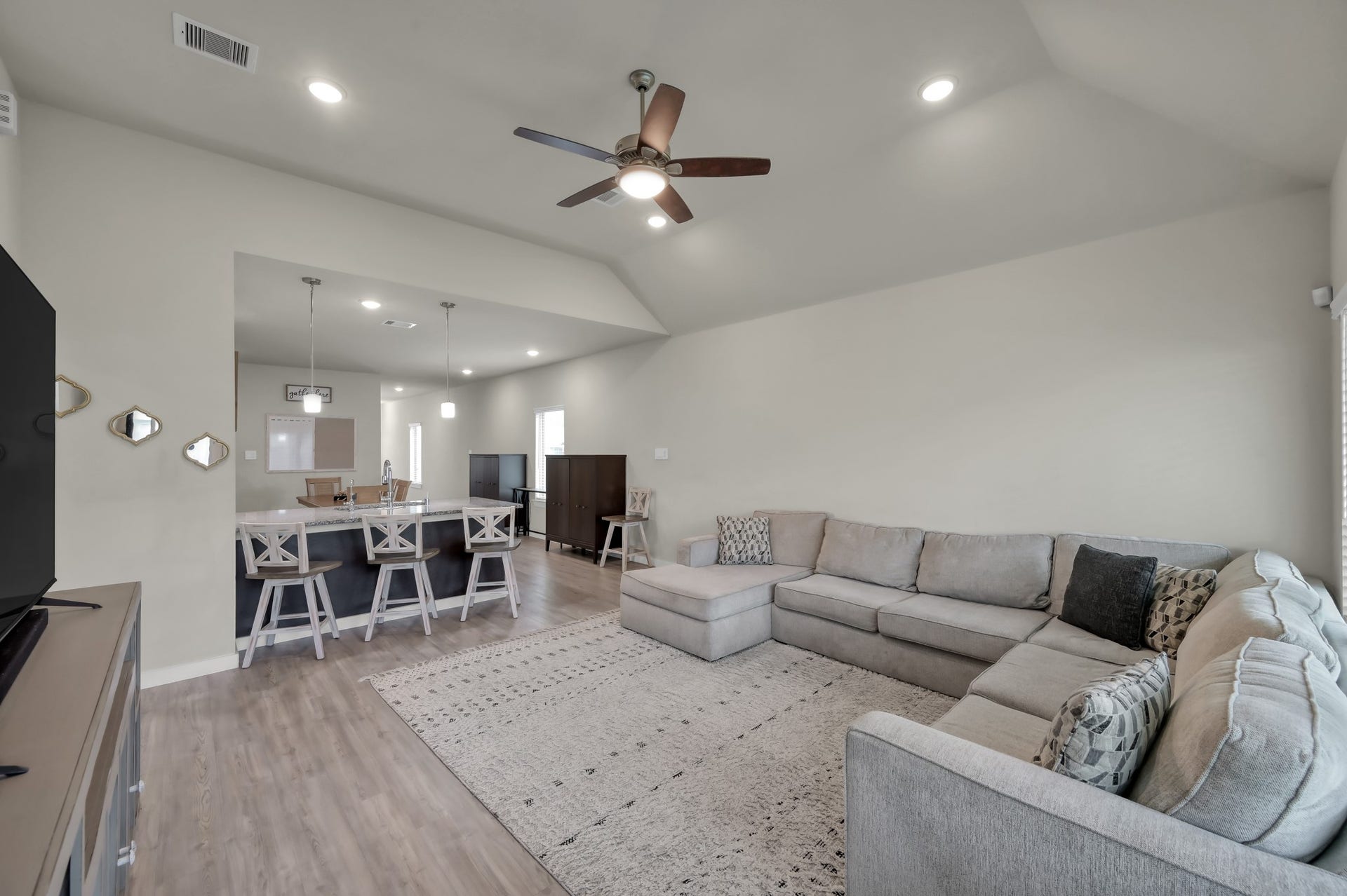 22203 Cardinal Crest Lane, New Caney, TX 77357 A spacious, open-concept living area featuring a large sectional sofa, modern ceiling fan, and recessed lighting. The room flows seamlessly into the kitchen, which has a breakfast bar with stylish pendant lights and seating. Neutral tones and sleek flooring enhance the contemporary feel.