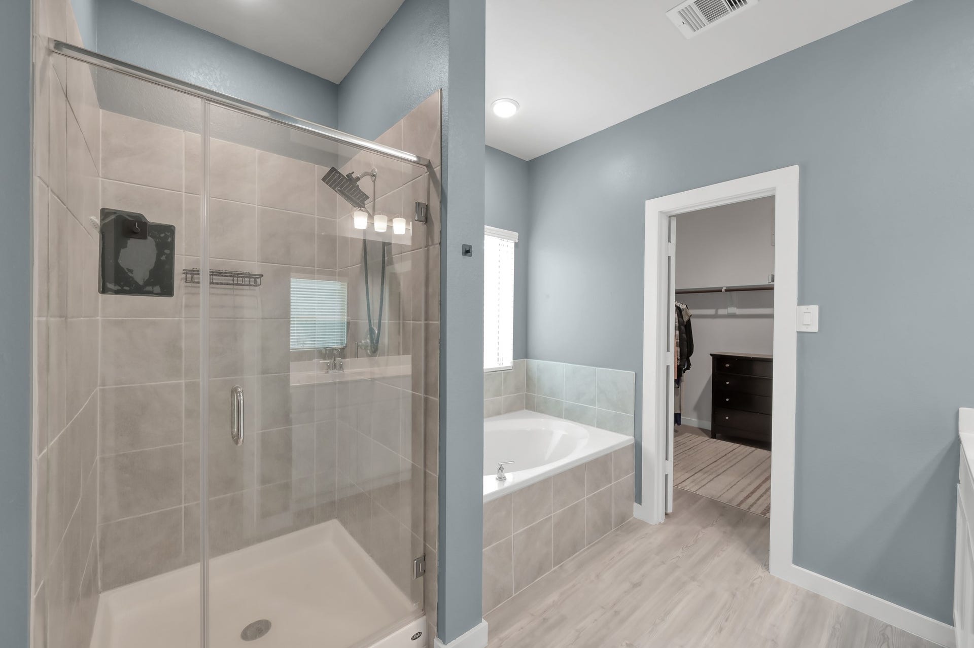 22203 Cardinal Crest Lane, New Caney, TX 77357 A modern bathroom featuring a glass-enclosed shower, a bathtub, and an adjoining walk-in closet. The room has a clean, contemporary design with light blue walls and ample natural light.