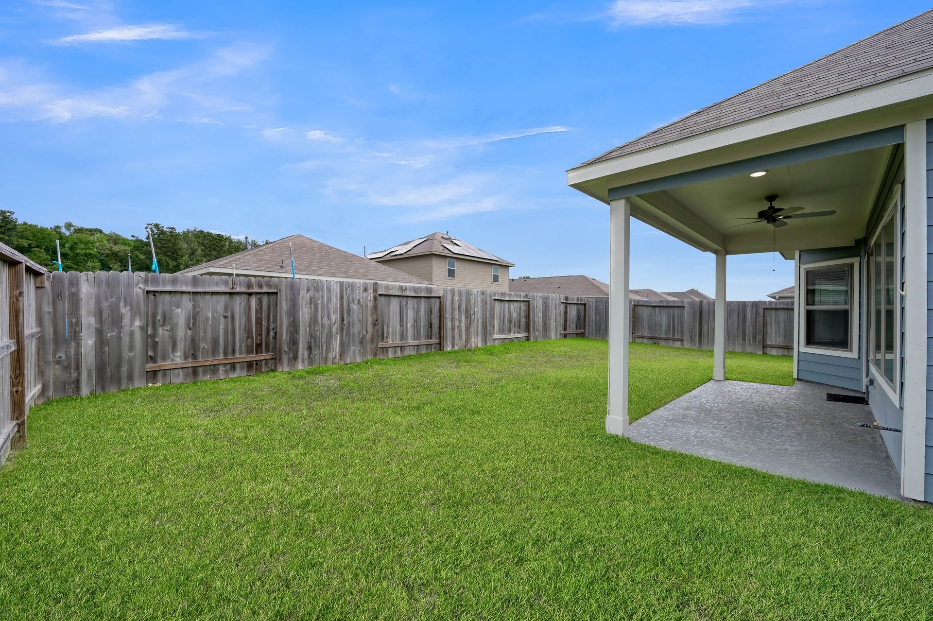 22203 Cardinal Crest Lane, New Caney, TX 77357 A spacious backyard with a well-maintained lawn, enclosed by a wooden fence for privacy. A covered patio area with a ceiling fan provides a comfortable spot for outdoor relaxation or entertaining.