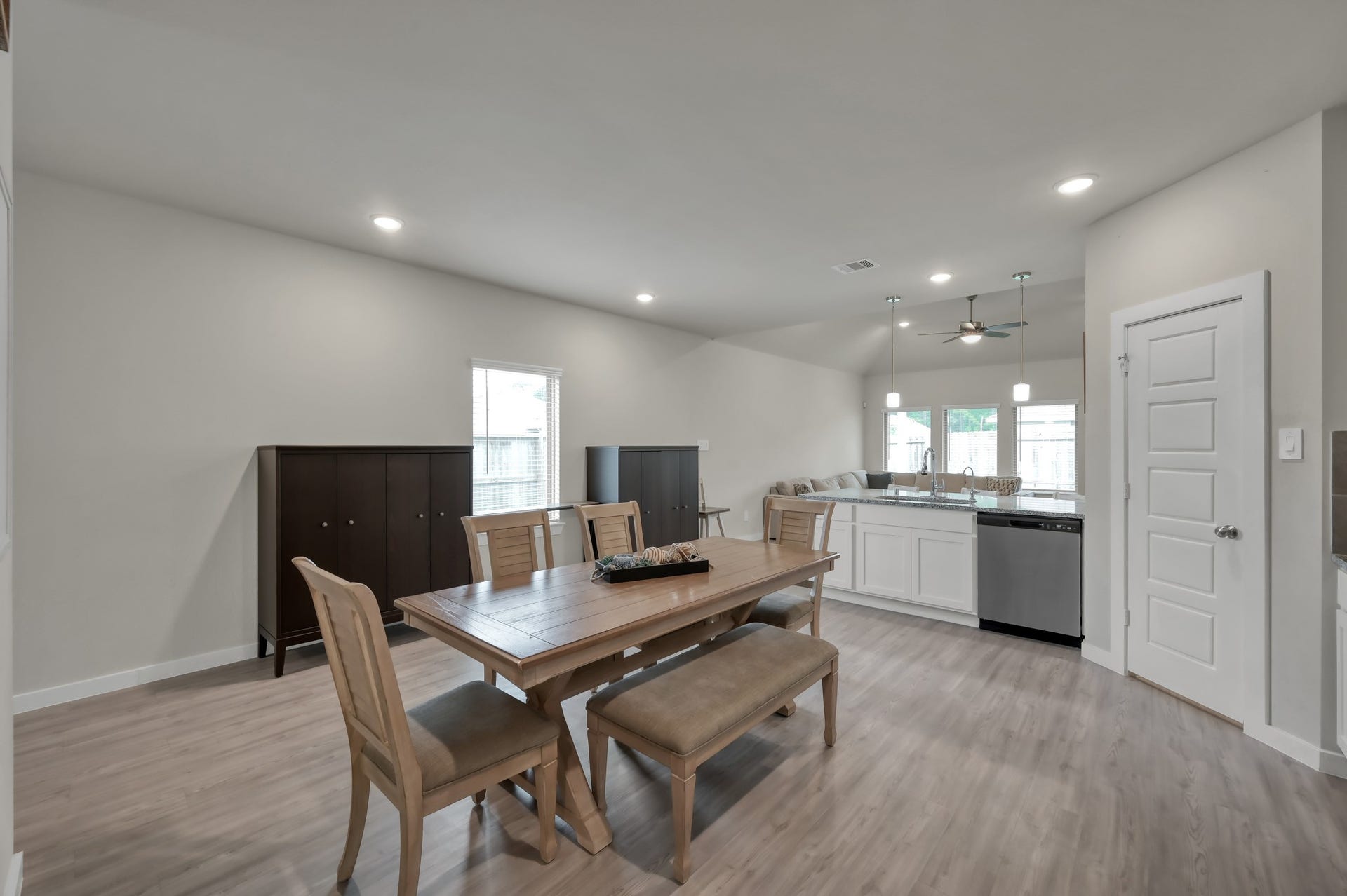 22203 Cardinal Crest Lane, New Caney, TX 77357 A modern, open-concept dining and kitchen area with a wooden dining set, light wood flooring, and neutral walls. The kitchen features white cabinetry, stainless steel appliances, and pendant lighting over the counter.