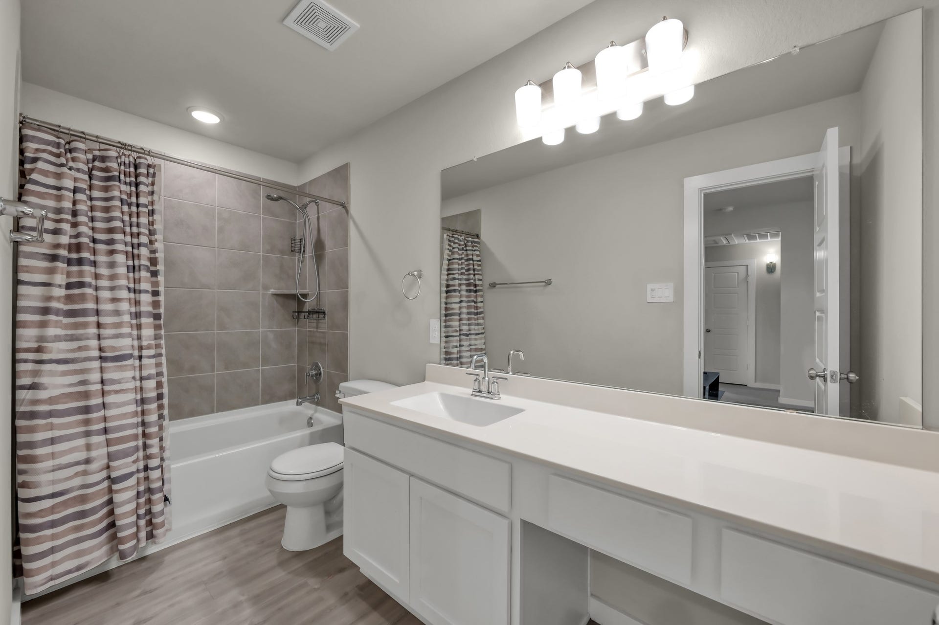 22203 Cardinal Crest Lane, New Caney, TX 77357 Modern bathroom featuring a large mirror, sleek vanity with ample counter space, and a full bathtub with a tiled shower area. Bright lighting and neutral tones create a clean, inviting atmosphere.