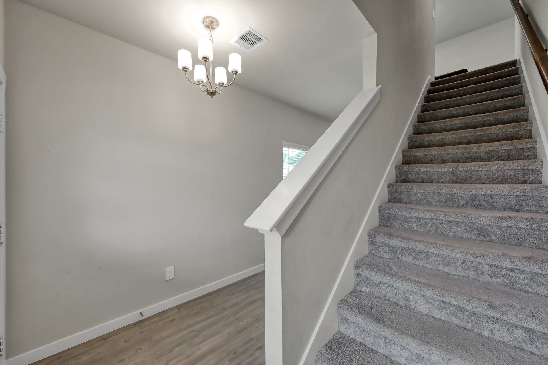 22203 Cardinal Crest Lane, New Caney, TX 77357 A modern, well-lit entryway with carpeted stairs leading to the upper floor. The space features light wood flooring and a simple chandelier for a welcoming ambiance.