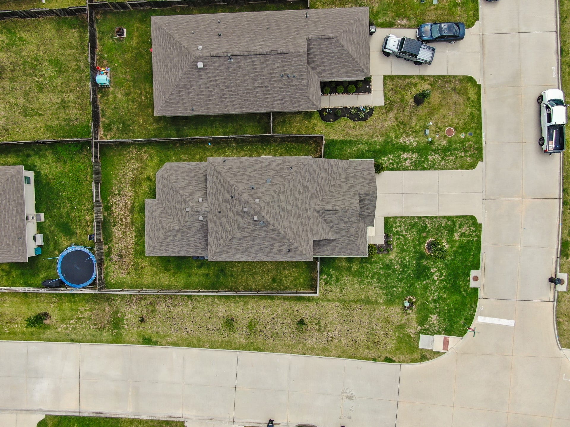 22203 Cardinal Crest Lane, New Caney, TX 77357 This aerial photo shows a suburban home with a large fenced backyard, a trampoline, and a driveway with parked vehicles. The house is situated on a corner lot in a neighborhood with similar homes.