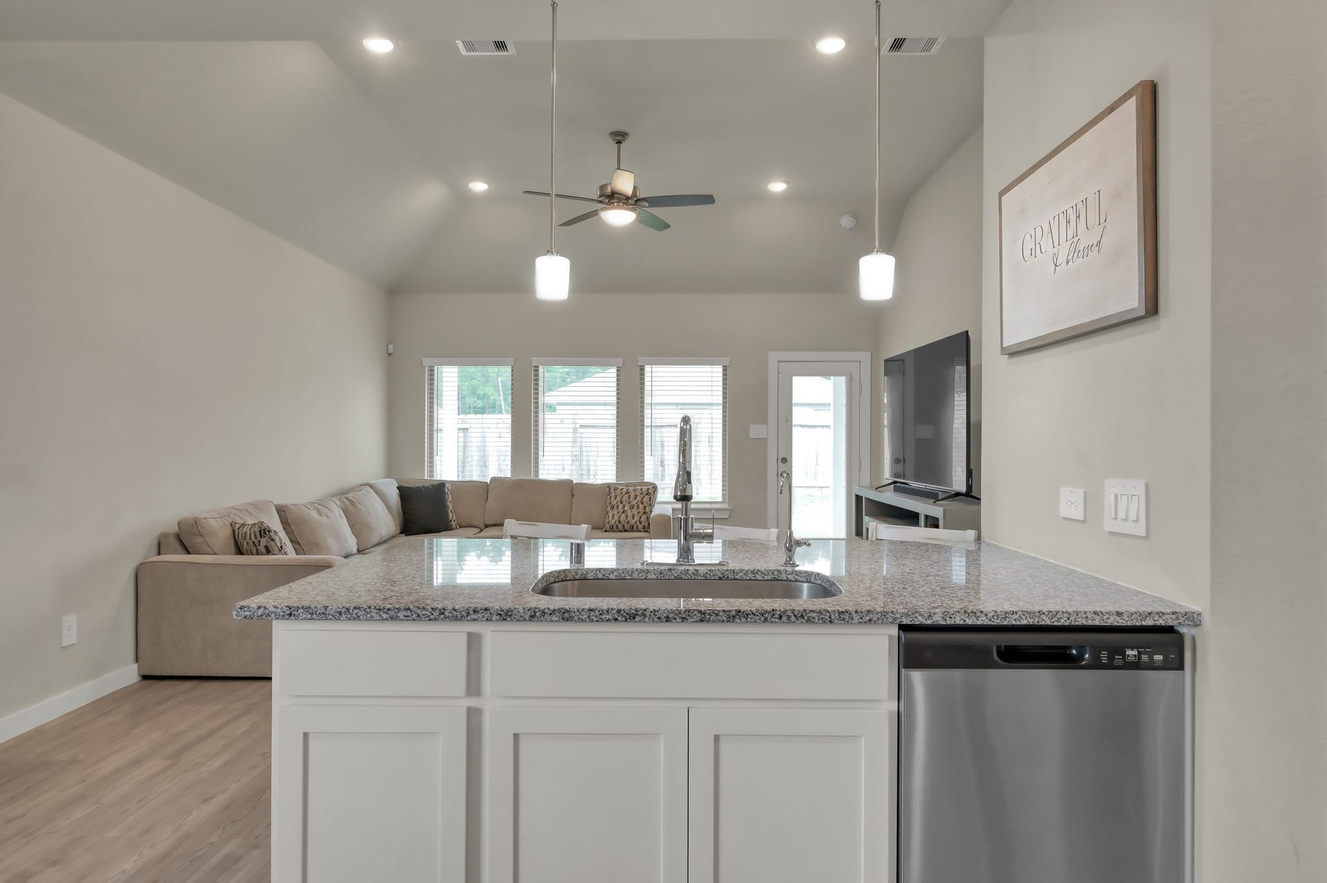 22203 Cardinal Crest Lane, New Caney, TX 77357 This spacious, open-concept living area features a modern kitchen with granite countertops and a central island, adjacent to a cozy living room with large windows and a ceiling fan.