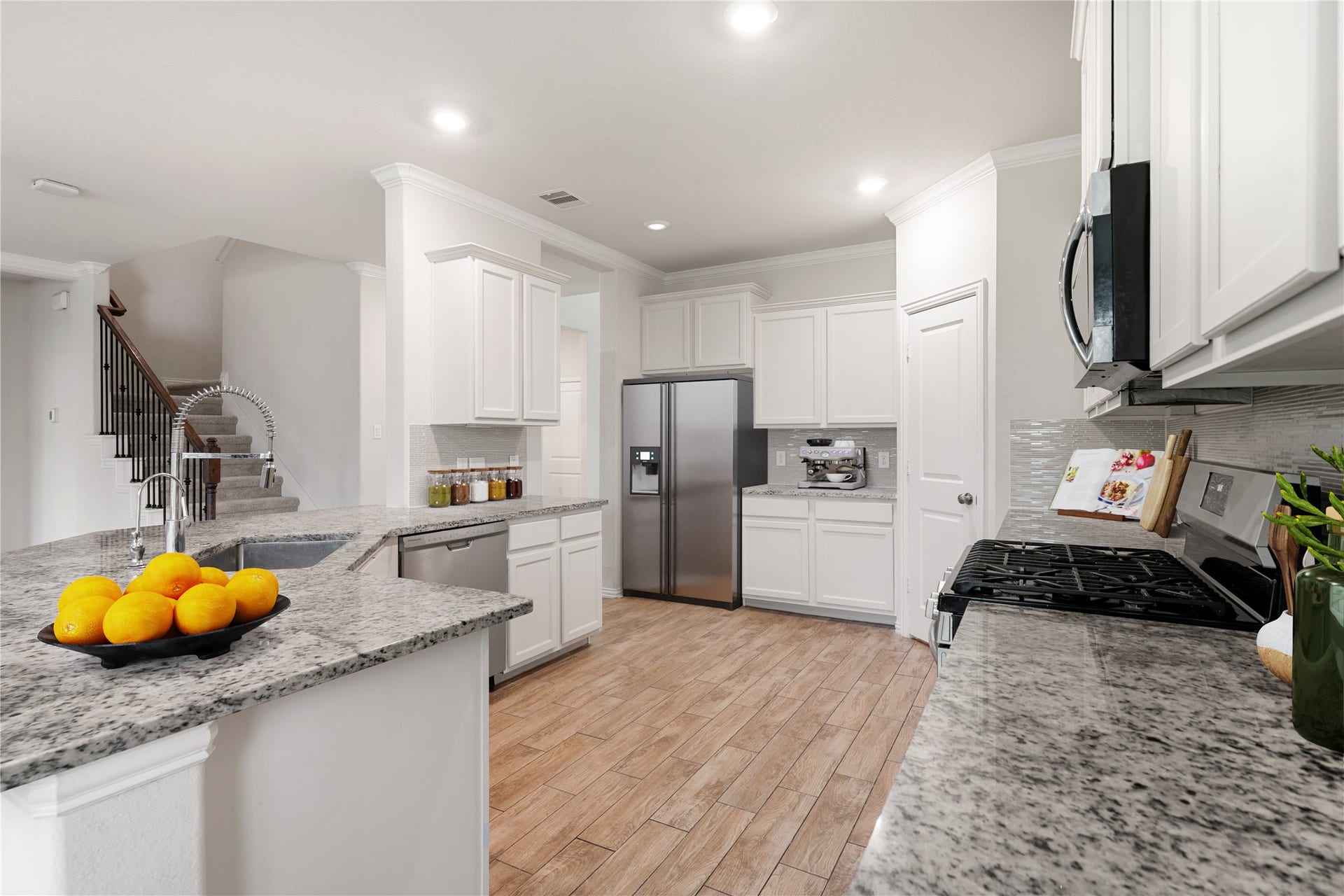 2418 Green Kale Drive, Richmond, TX 77406 Beautifully designed and full of function, this kitchen offers ample white cabinetry, granite countertops, a tile backsplash, stainless steel appliances including a gas range, and rich wood-look tile flooring throughout, with the staircase conveniently nearby. *Virtually Staged