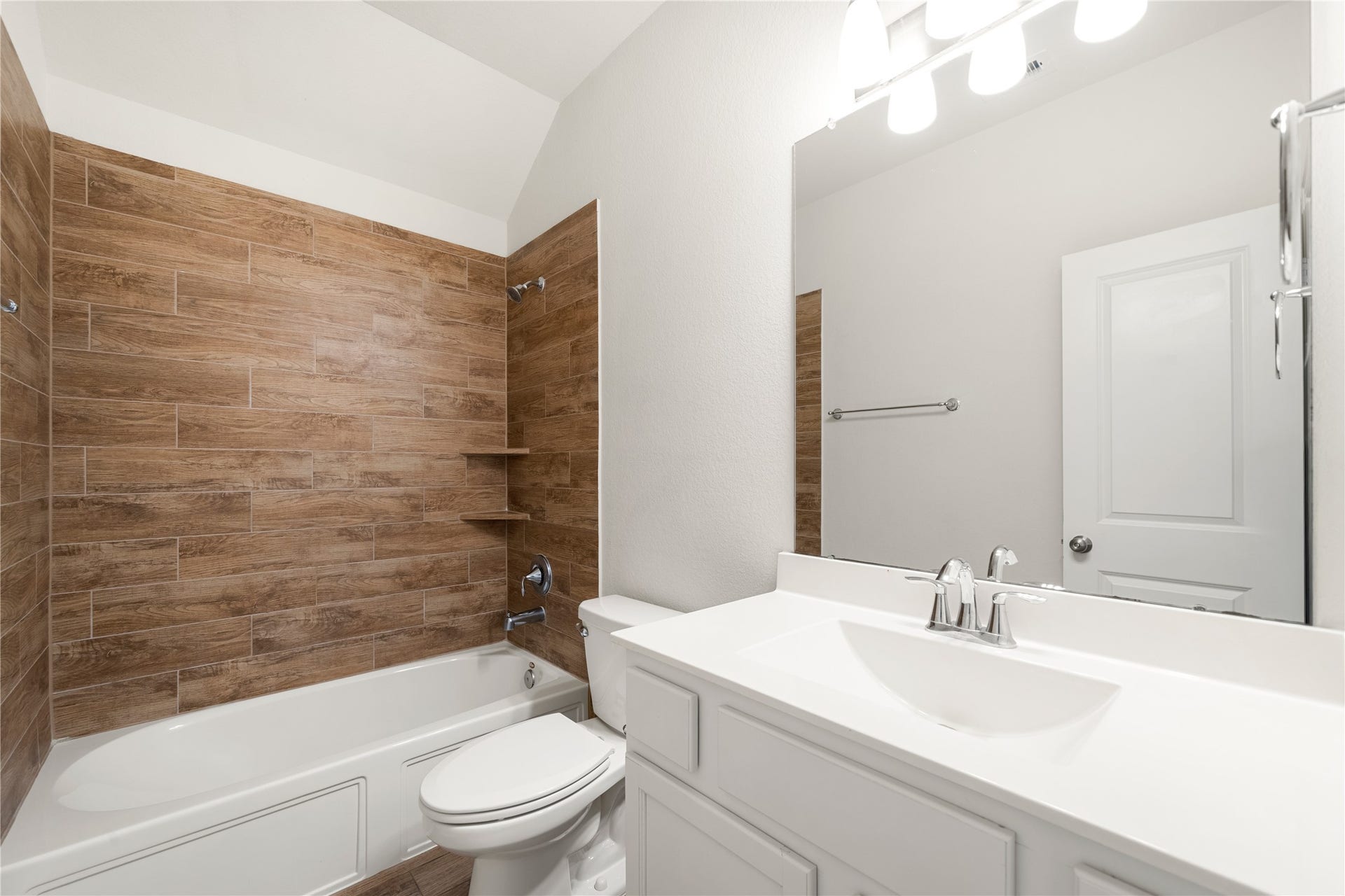 2418 Green Kale Drive, Richmond, TX 77406 Another stylish full bath featuring a white vanity, large mirror, vaulted ceiling, and a tub/shower combo with rich wood-look tile surround!