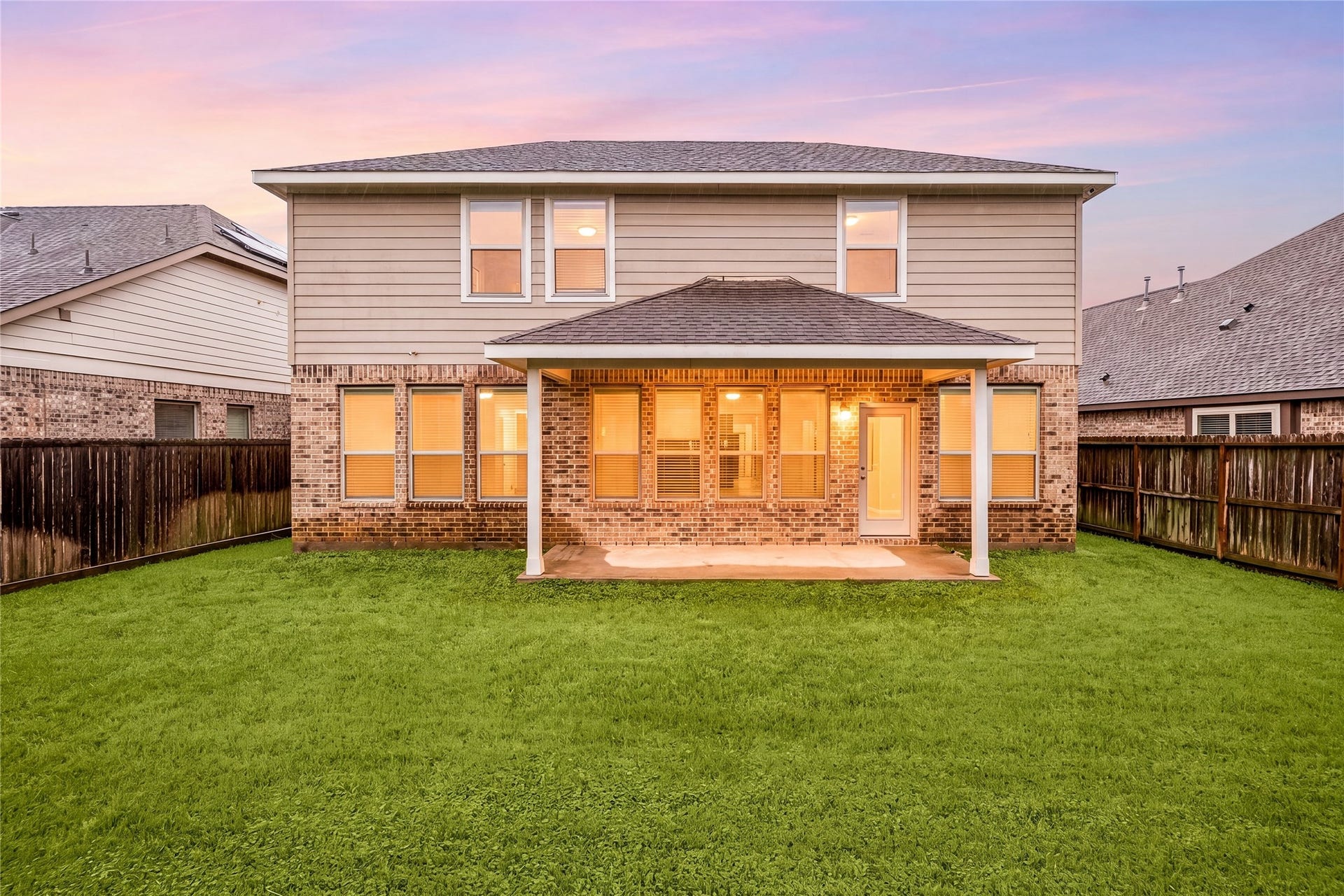 2418 Green Kale Drive, Richmond, TX 77406 As the sun sets, the home glows with warmth and charm! This stunning rear view showcases the spacious covered patio, lush fenced backyard, and beautiful brick elevation, the perfect setting to relax and enjoy those Texas evenings.