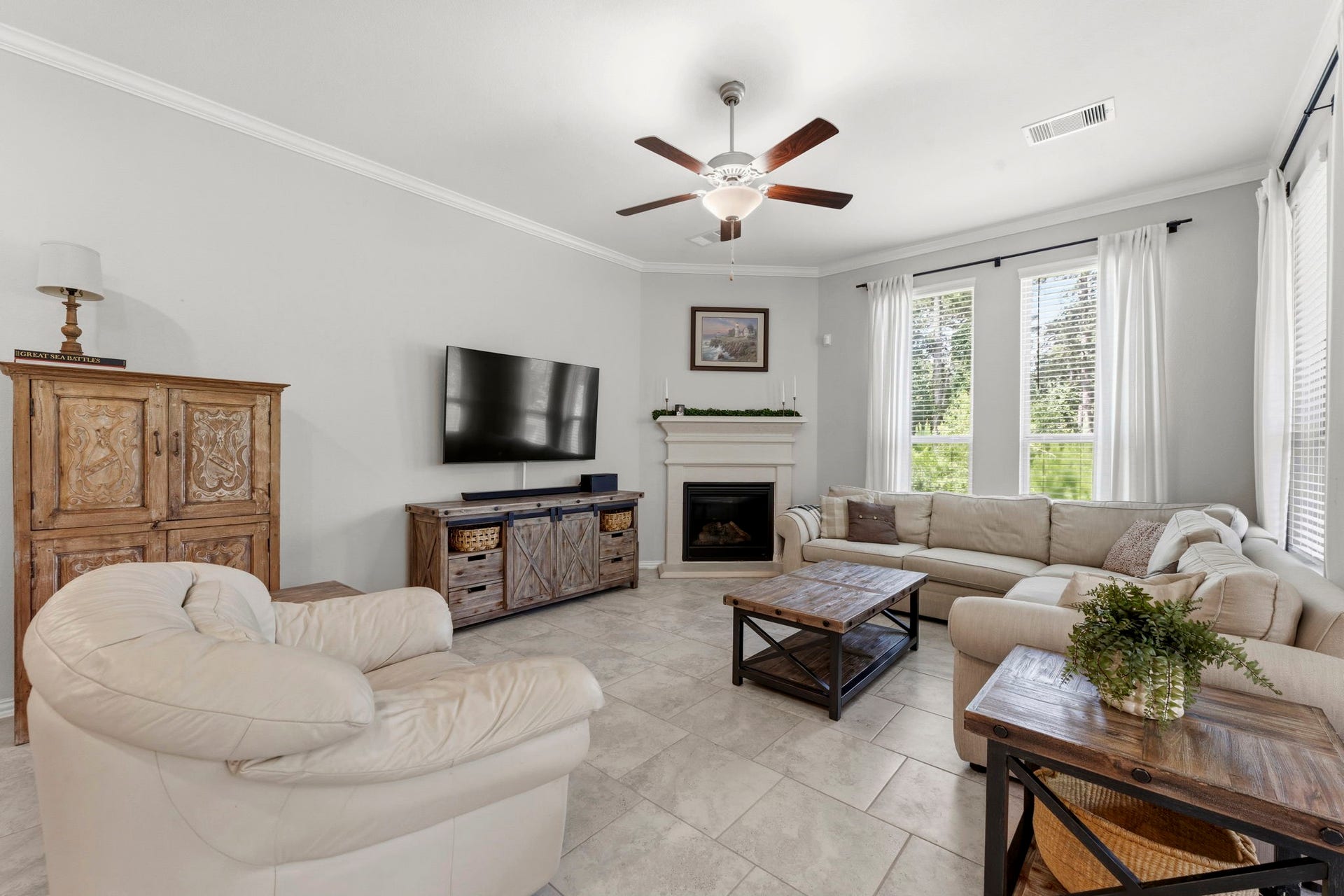 2143 Moss Creek Lane, Conroe, TX 77304 Light-filled living room featuring elevated ceilings, crown molding, a cozy fireplace, and a wall of windows overlooking the backyard.