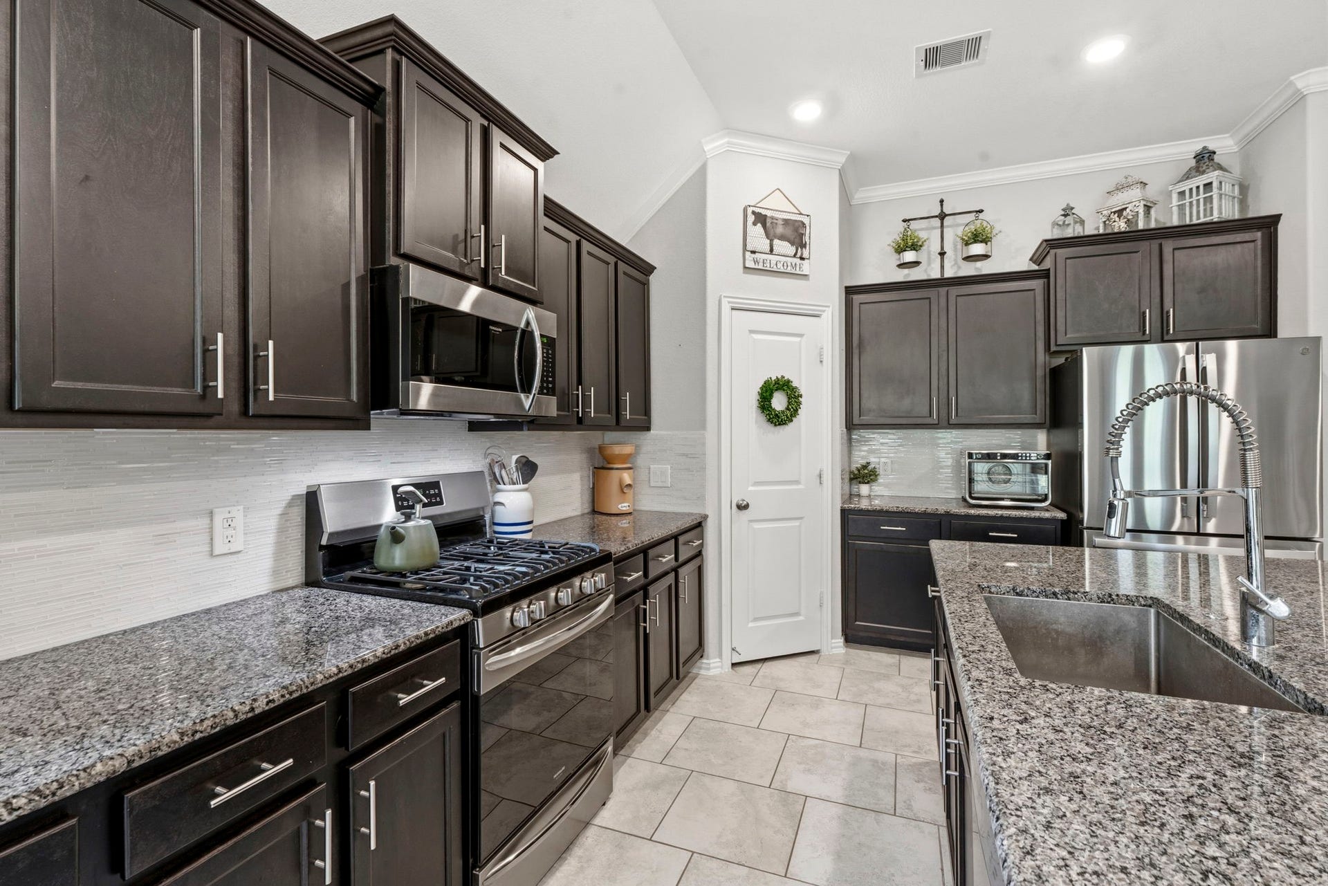 2143 Moss Creek Lane, Conroe, TX 77304 The beautifully appointed kitchen features an oversized island with breakfast bar, granite countertops, stainless steel appliances, a gas cooktop, and a walk-in pantry. Enjoy clean, fresh water throughout the home with the added convenience of a whole-house water filtration system.