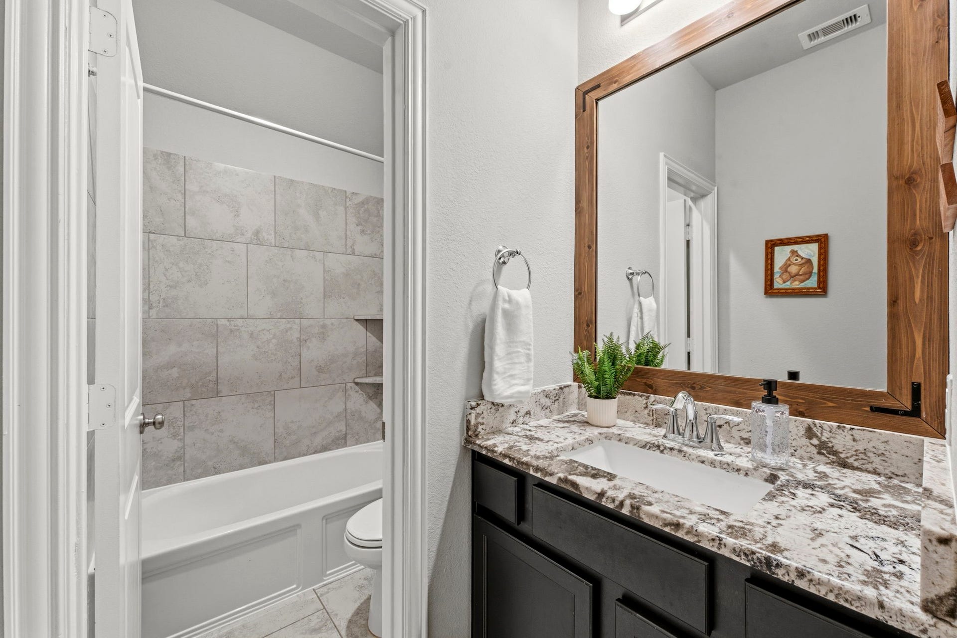 2143 Moss Creek Lane, Conroe, TX 77304 The first hall bathroom features an upgraded granite countertop, a custom framed mirror, and elegant finishes.