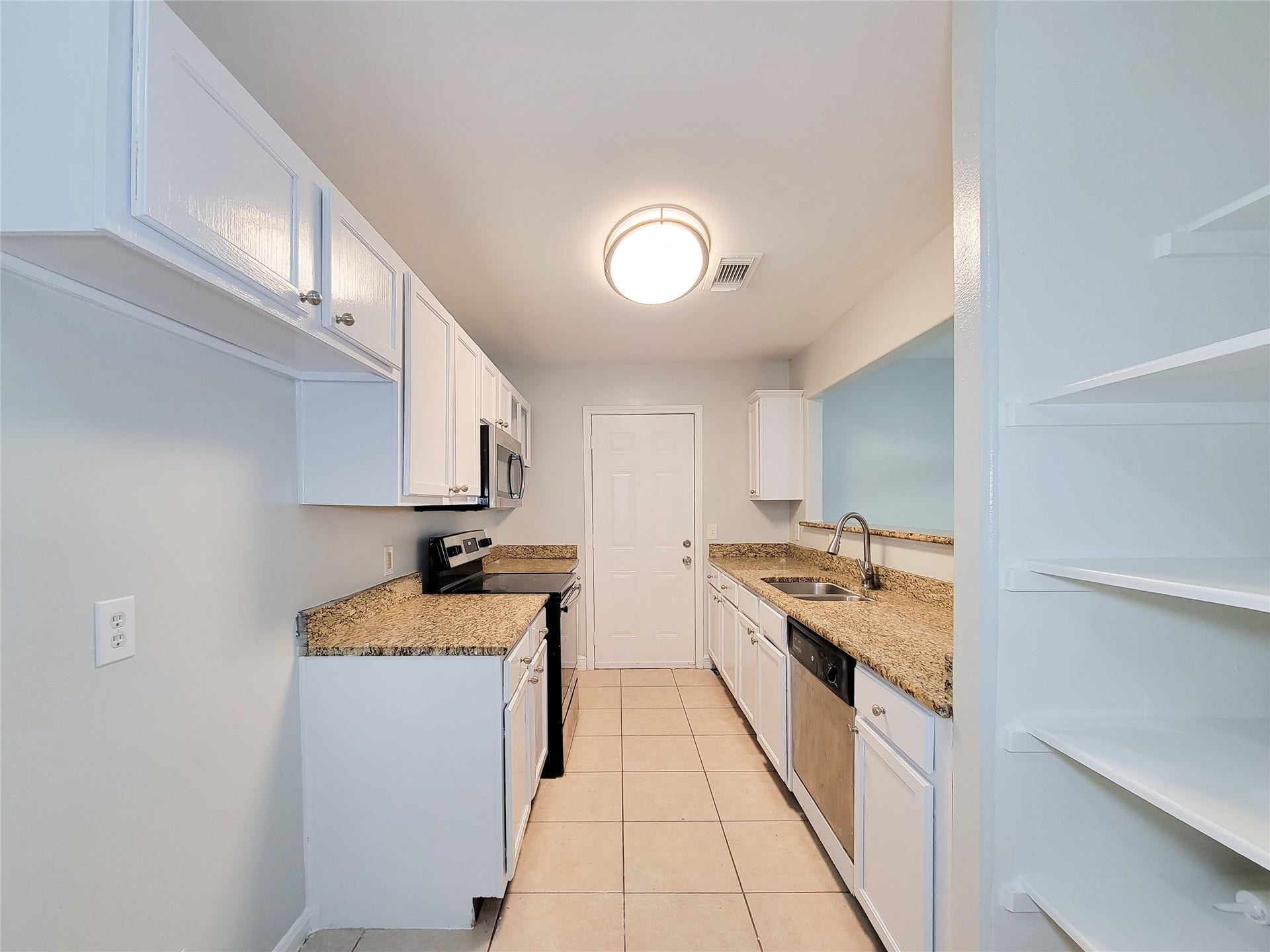 3005 La Estancia Lane, Houston, TX 77093 Bright galley kitchen featuring granite countertops, stainless steel appliances, and ample cabinet storage, complemented by a convenient open shelving unit.