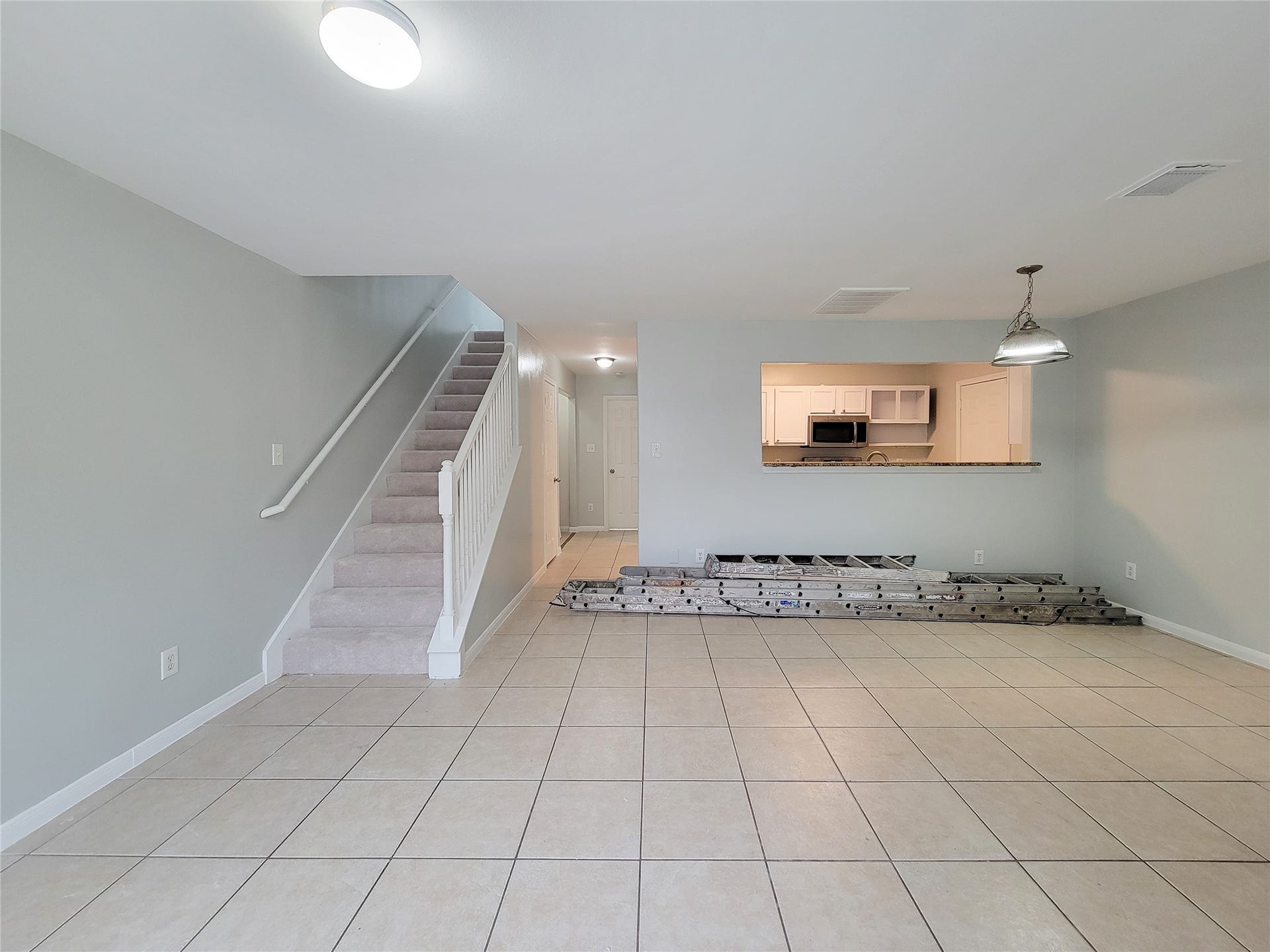 3005 La Estancia Lane, Houston, TX 77093 Spacious open-plan living area with neutral tile flooring, leading to a cozy carpeted staircase, and featuring a modern kitchen with a convenient pass-through window.