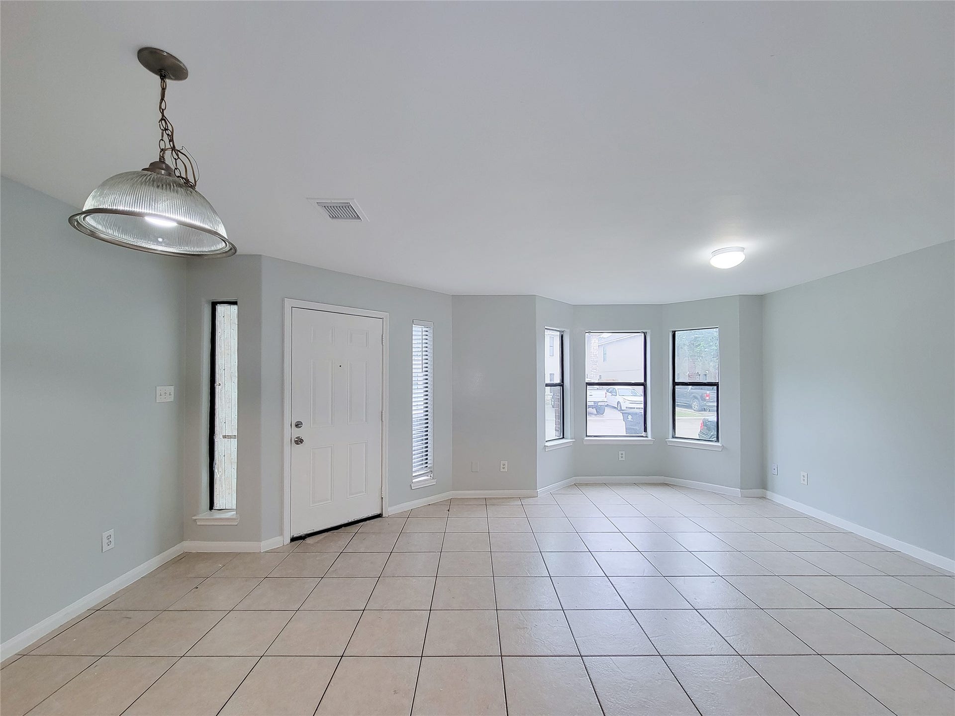 3005 La Estancia Lane, Houston, TX 77093 Spacious and bright living area with large windows, neutral tile flooring, and a stylish overhead light fixture, perfect for versatile decorating.
