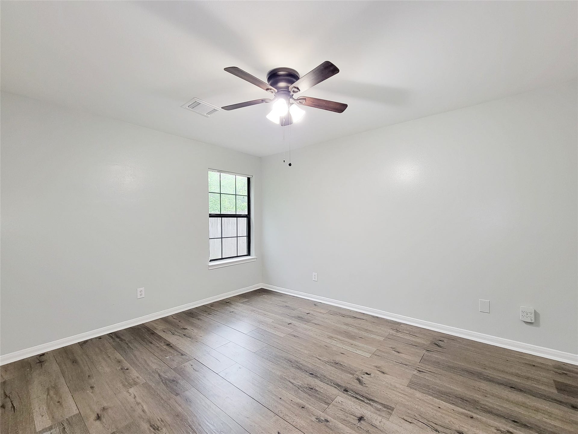 3005 La Estancia Lane, Houston, TX 77093 Spacious bedroom featuring elegant wood flooring, a modern ceiling fan, and abundant natural light from the large window.