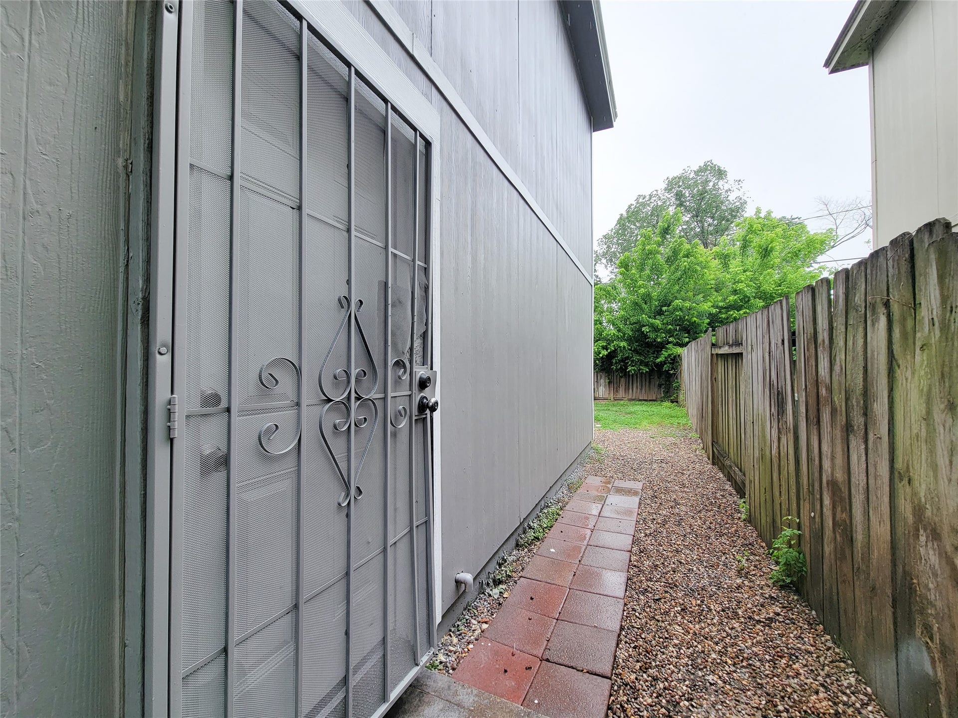 3005 La Estancia Lane, Houston, TX 77093 Charming side yard with a secure wrought iron door, offering privacy and a pathway leading to a cozy backyard space.