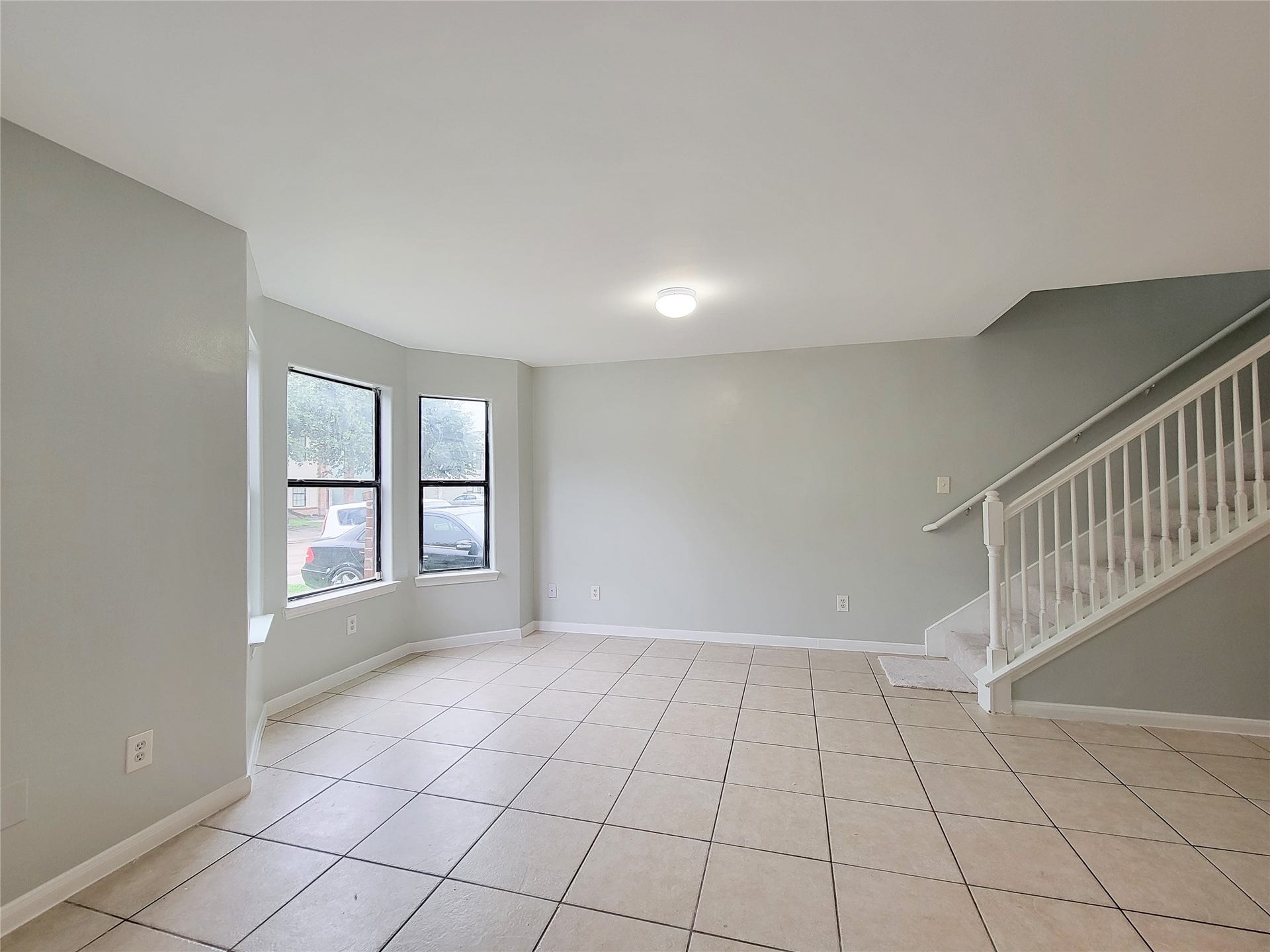 3005 La Estancia Lane, Houston, TX 77093 Spacious living area with abundant natural light, featuring a charming bay window and easy-to-maintain tile flooring, complemented by a staircase leading to the upper level.