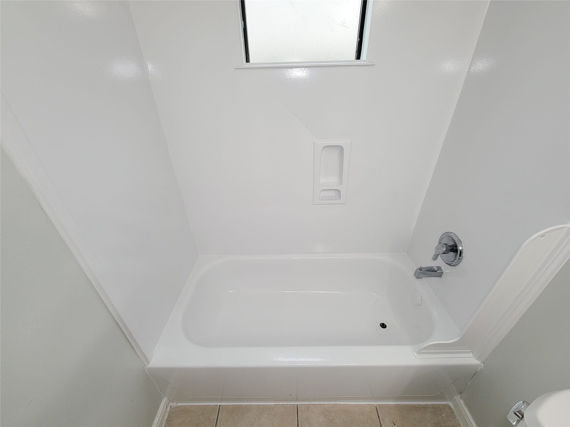 3005 La Estancia Lane, Houston, TX 77093 Modern bathroom featuring a pristine white bathtub with sleek fixtures, complemented by neutral tile flooring and a frosted window for privacy.