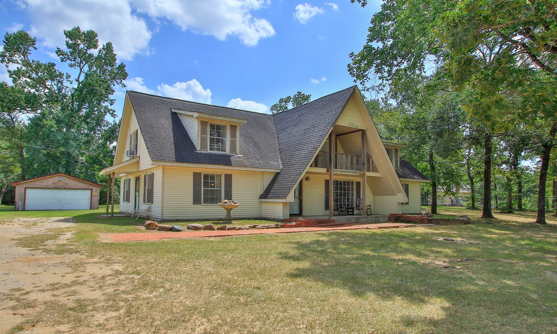 AMAZING 5 ACRE LOT. Main home nestled in a wooded setting, featuring a spacious front porch, front balcony, shop, space for animals, and a detached two-car garage.