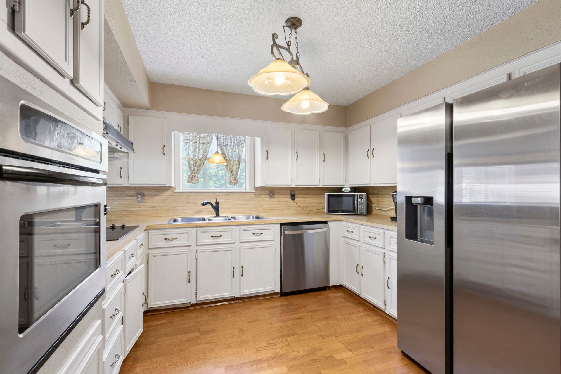 A charming kitchen filled with warmth and light.
White cabinetry and stainless steel appliances create a bright, inviting space ready for everyday meals, entertaining, and culinary creativity. The countertop microwave can stay with the home.