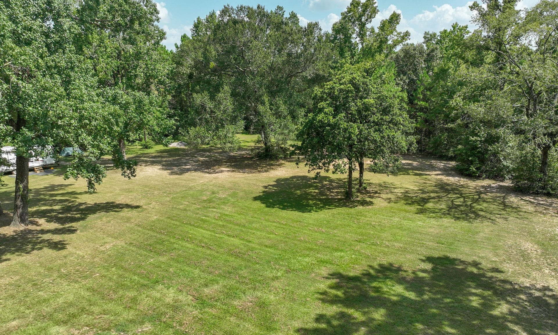 5 ACRES - Expansive, lush green lawn surrounded by mature trees offers a serene and private setting, perfect for outdoor activities and relaxation. Land extends into the back treeline.
