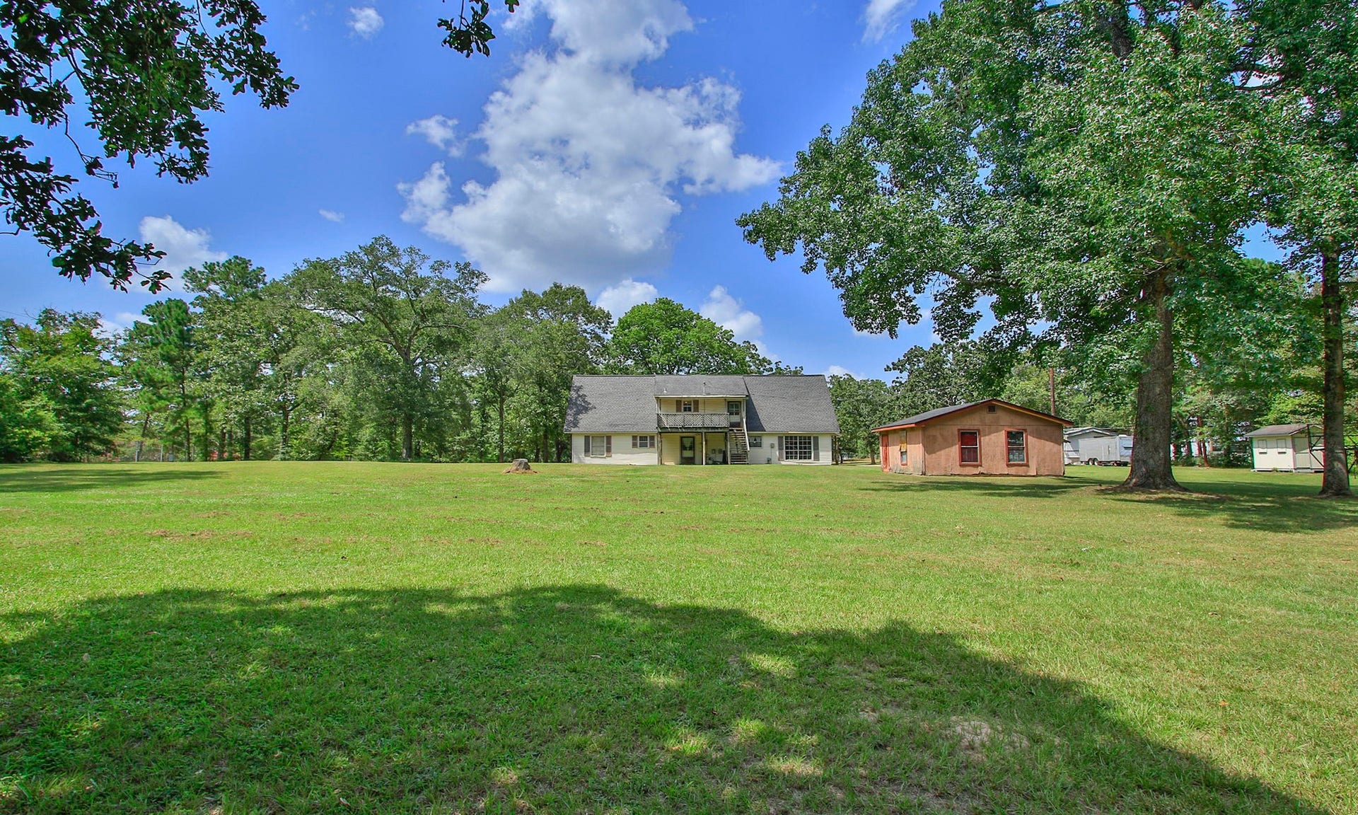Large, mature trees are scattered throughout the acreage, creating a peaceful country setting with a private well, workshop, chicken coop, and plenty of outdoor storage space.