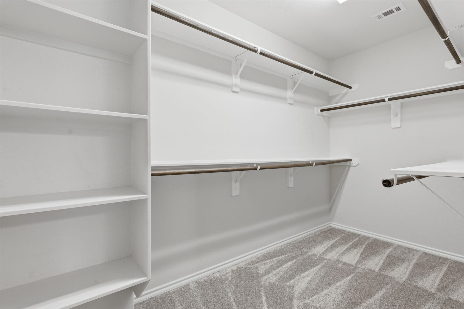 4028 Starbright Street, Houston, TX 77018 Expansive walk-in closet is fully equipped with built-in wooden shelving and multiple hanging rods over neutral carpet flooring.