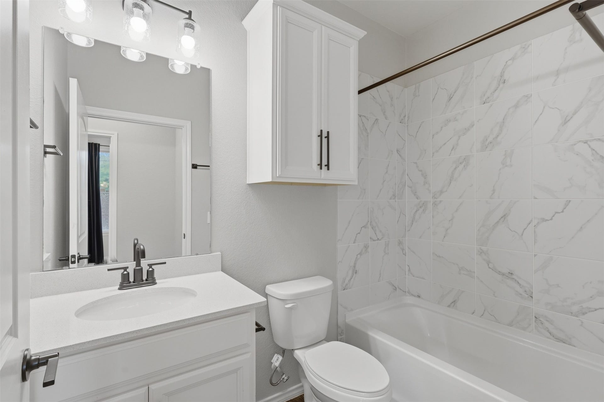 4028 Starbright Street, Houston, TX 77018 Modern secondary bathroom with a white vanity, matching cabinetry, large mirror with contemporary lighting, and a tub with marble-patterned tile surround.