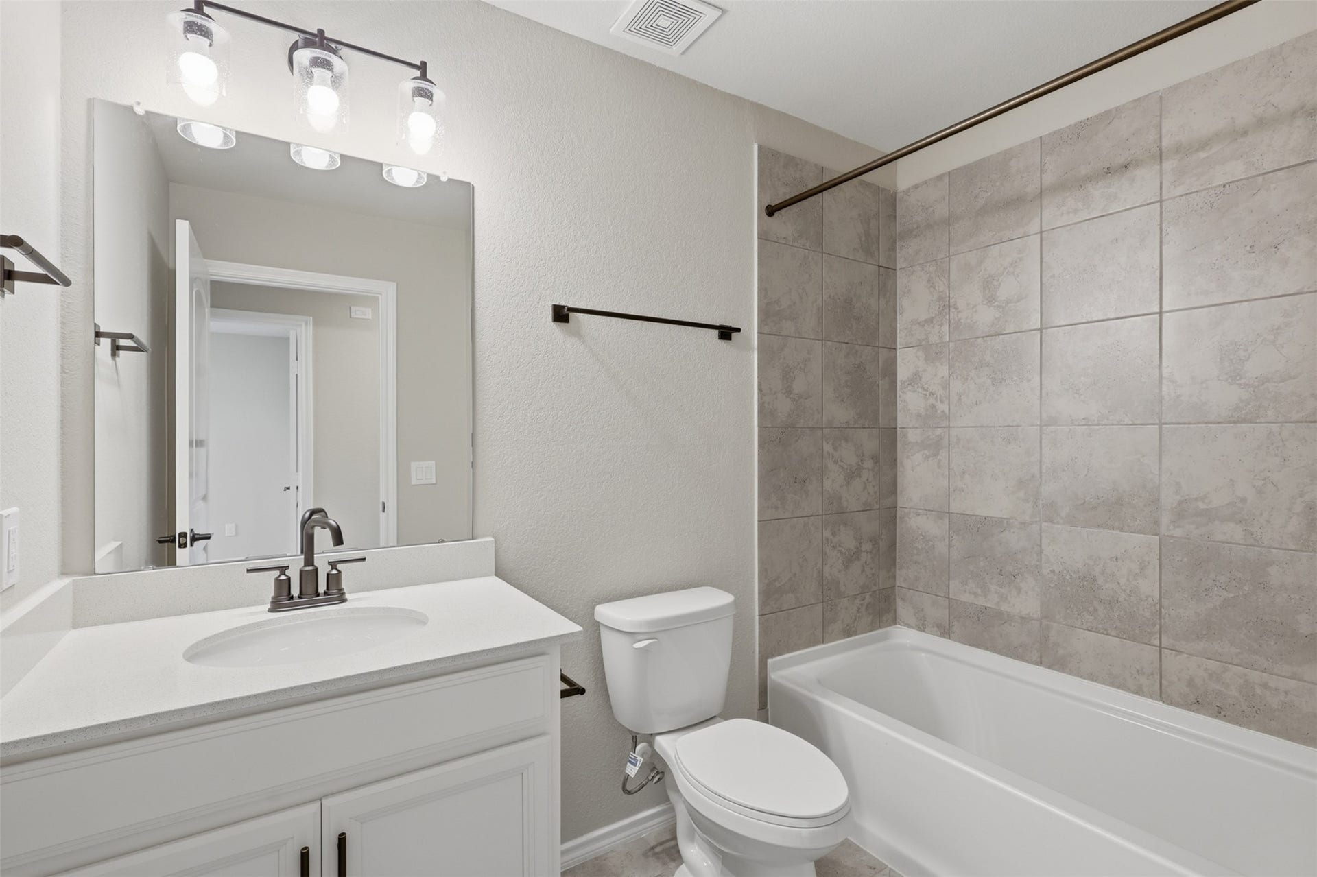 4028 Starbright Street, Houston, TX 77018 This full bathroom features a crisp white vanity paired with a neutral tiled tub shower combination and contemporary dark hardware.
