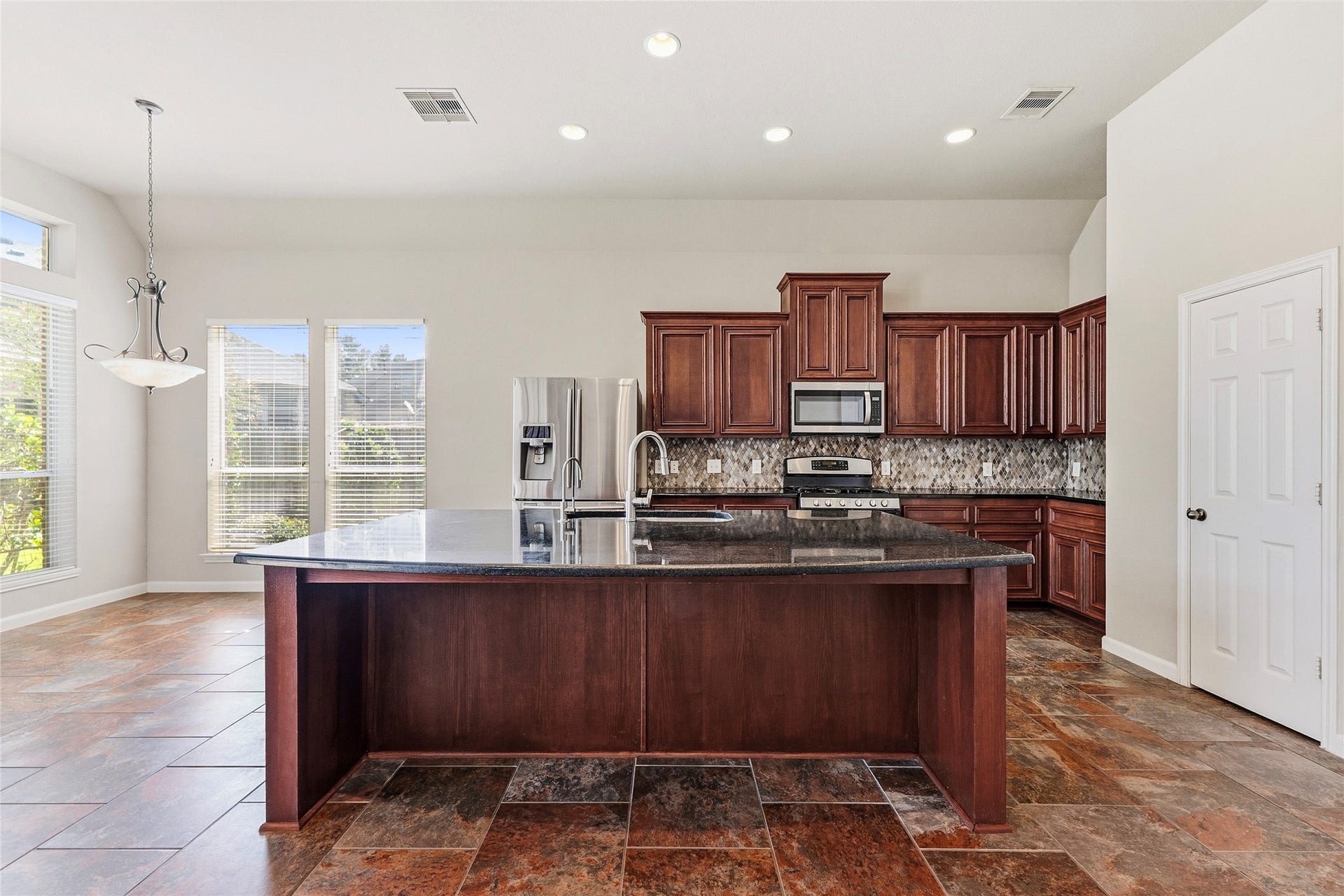 Spacious kitchen with elegant dark wood cabinetry, a large granite island, and stainless steel appliances, complemented by abundant natural light from the large windows.