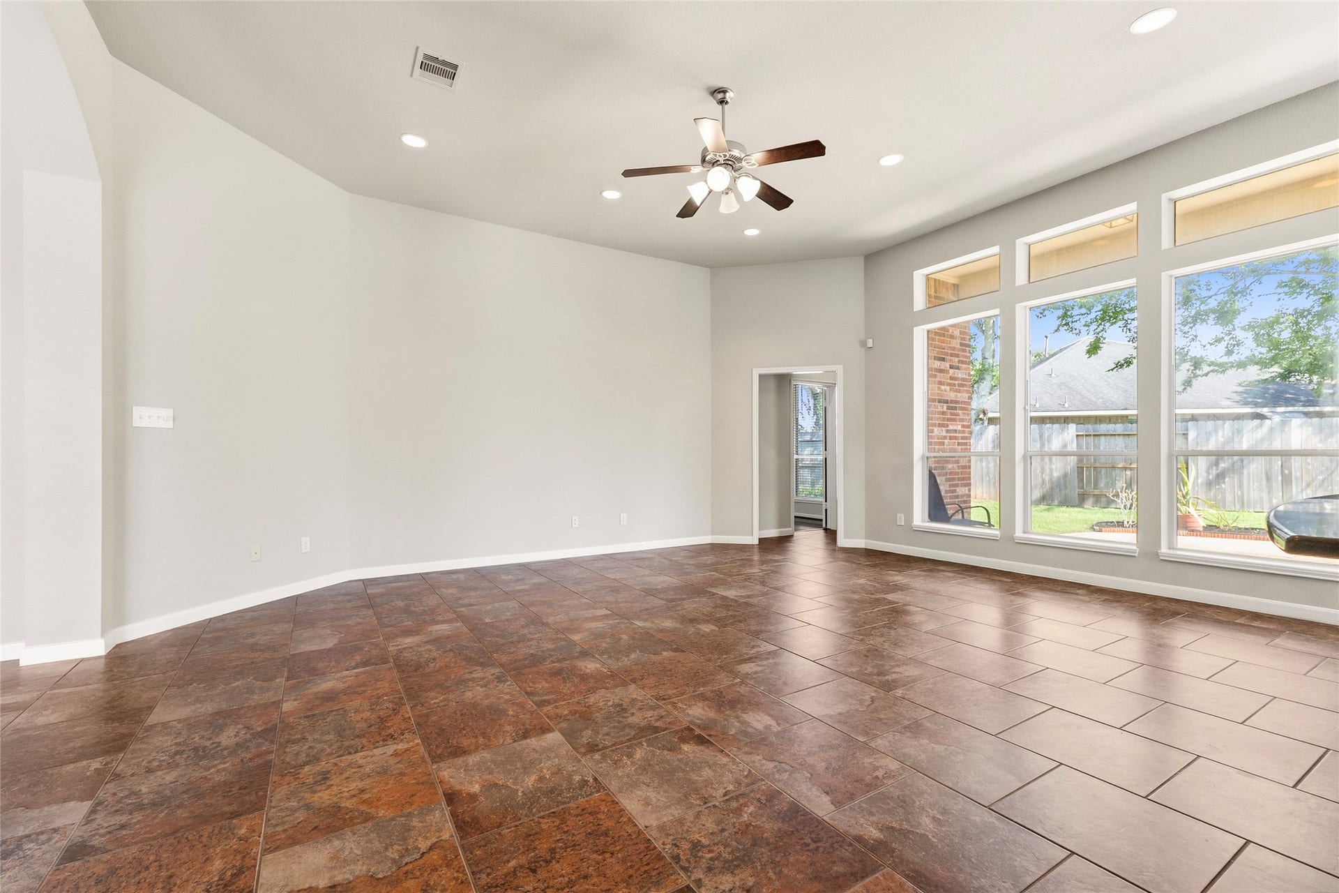 Spacious living area with elegant tile flooring, abundant natural light from large windows, and a modern ceiling fan, perfect for gatherings and relaxation.