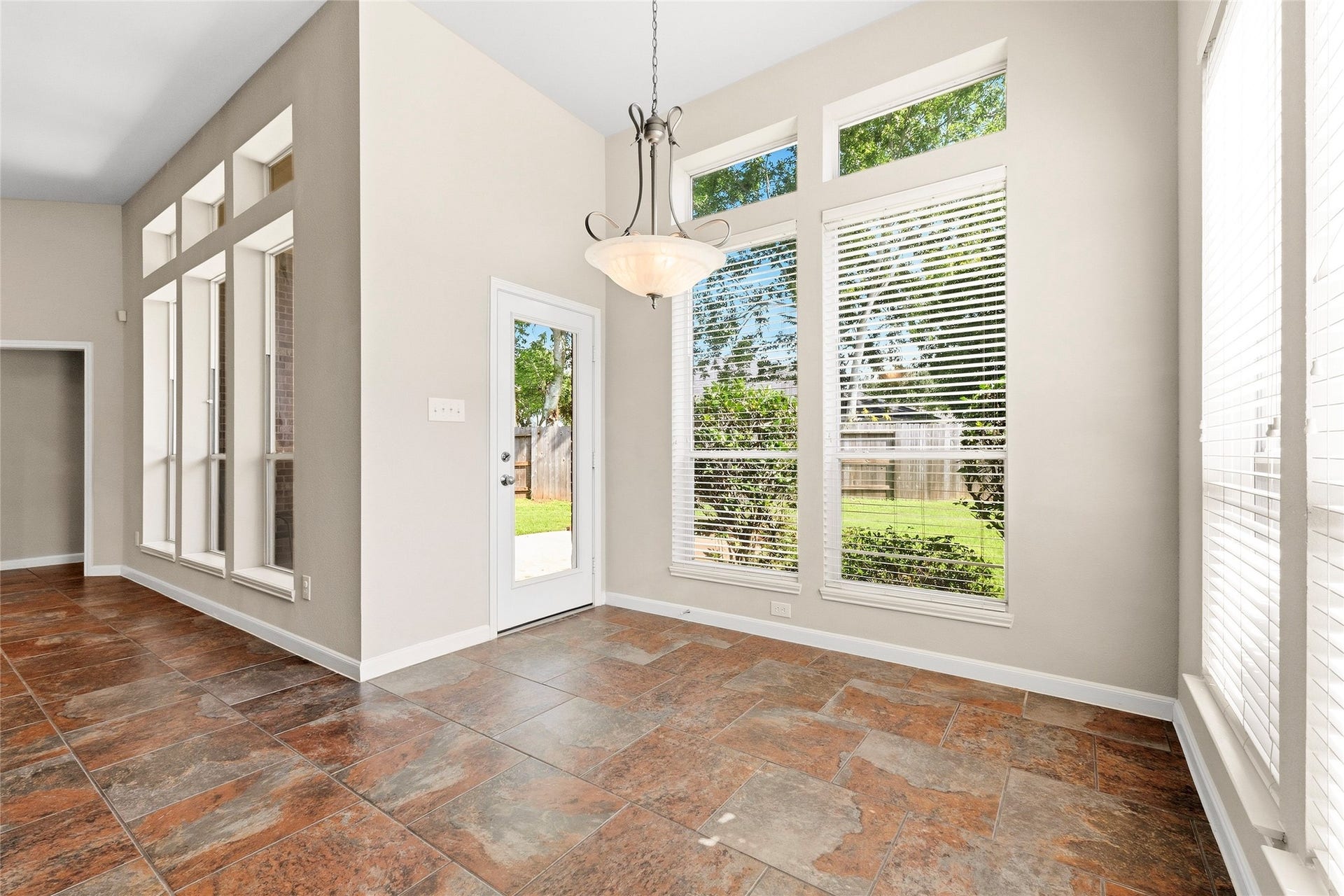 Bright and airy breakfast with large windows, high ceilings, and elegant tile flooring, offering a perfect view of the lush backyard.