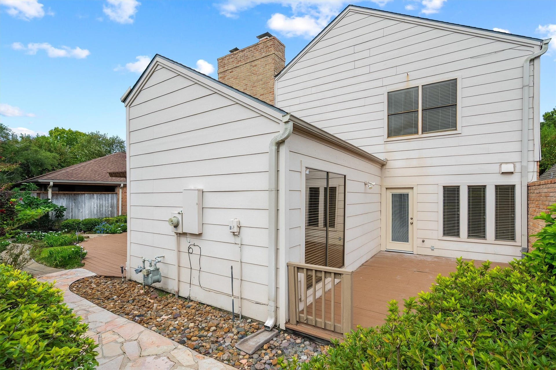 12219 Ravenmoor Drive, Houston, TX 77077 Charming two-story home featuring a spacious wooden deck, perfect for outdoor gatherings, surrounded by lush greenery and a well-maintained garden path.