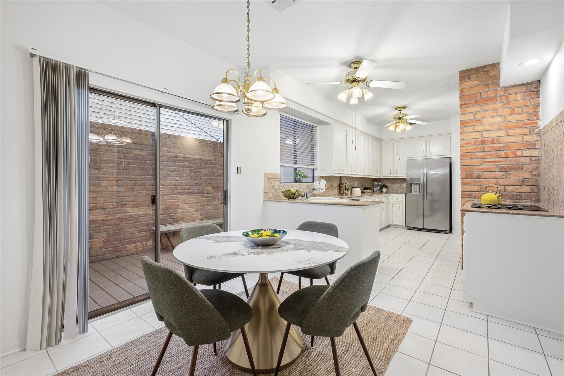 12219 Ravenmoor Drive, Houston, TX 77077 Bright and inviting kitchen-dining area featuring sleek stainless steel appliances, and a charming brick accent wall, all enhanced by ample natural light from large sliding glass doors.