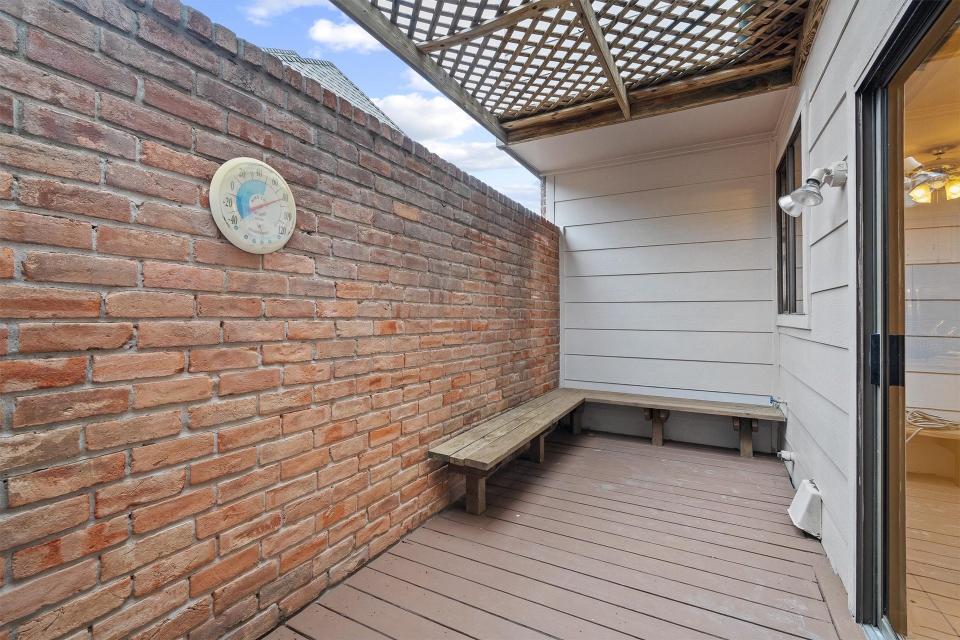 12219 Ravenmoor Drive, Houston, TX 77077 Charming private patio with a rustic brick wall, cozy bench seating, and a lattice roof, perfect for relaxing and enjoying the outdoors.