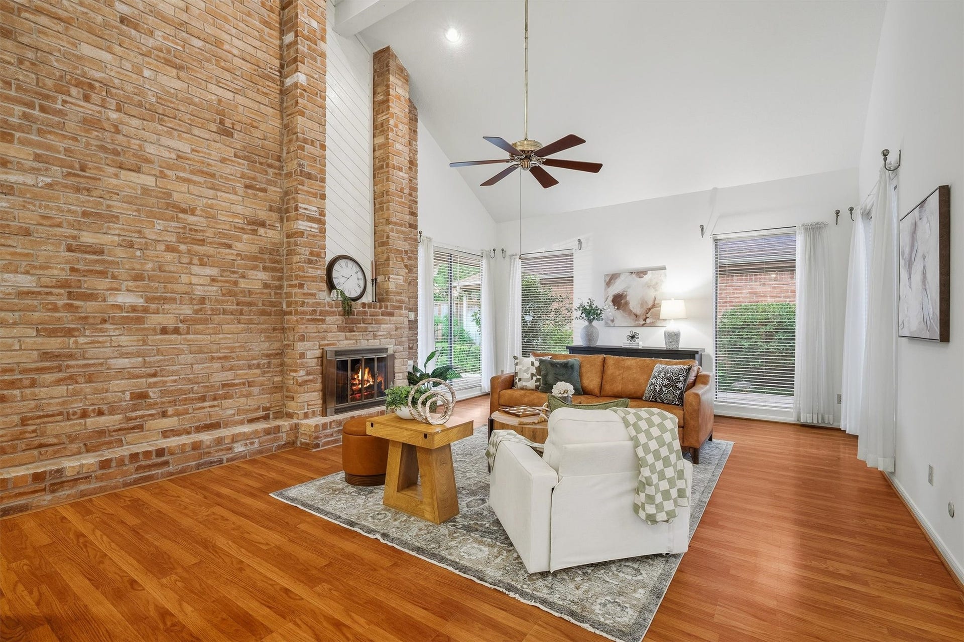 12219 Ravenmoor Drive, Houston, TX 77077 Inviting living room with a stunning brick fireplace, vaulted ceilings, and abundant natural light from large windows, offering a warm and spacious atmosphere.
