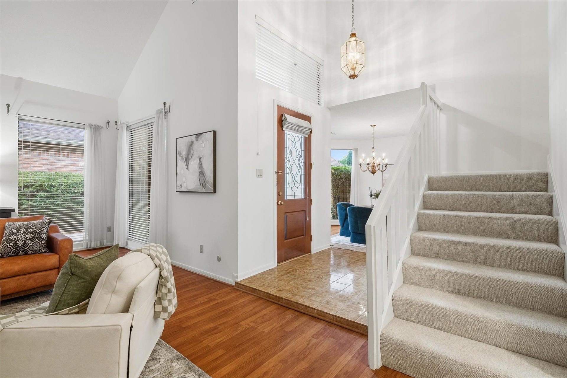 12219 Ravenmoor Drive, Houston, TX 77077 Bright and welcoming entryway with a carpeted staircase, hardwood floors, and a chandelier-lit dining area, leading to a cozy living space with large windows.