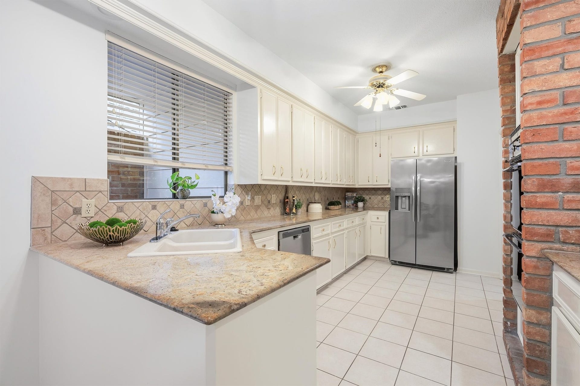 12219 Ravenmoor Drive, Houston, TX 77077 Spacious kitchen with elegant granite countertops, classic white cabinetry, and modern stainless steel appliances, complemented by a charming brick accent wall.