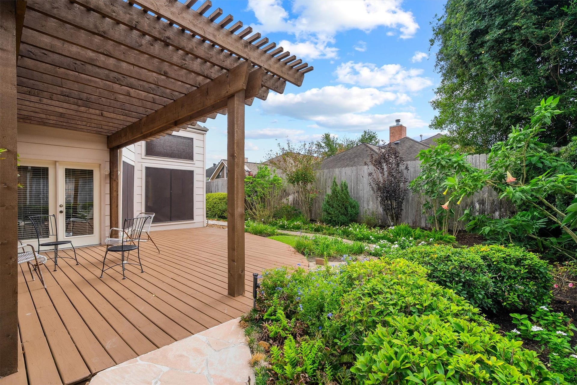 12219 Ravenmoor Drive, Houston, TX 77077 Experience serene outdoor living with this charming wooden deck featuring a pergola, surrounded by lush greenery and vibrant gardens.