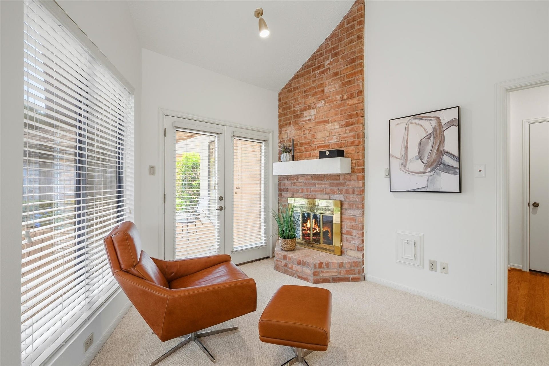 12219 Ravenmoor Drive, Houston, TX 77077 Cozy living space featuring a charming brick fireplace, abundant natural light from large windows and French doors, and a stylish leather chair perfect for relaxation.
