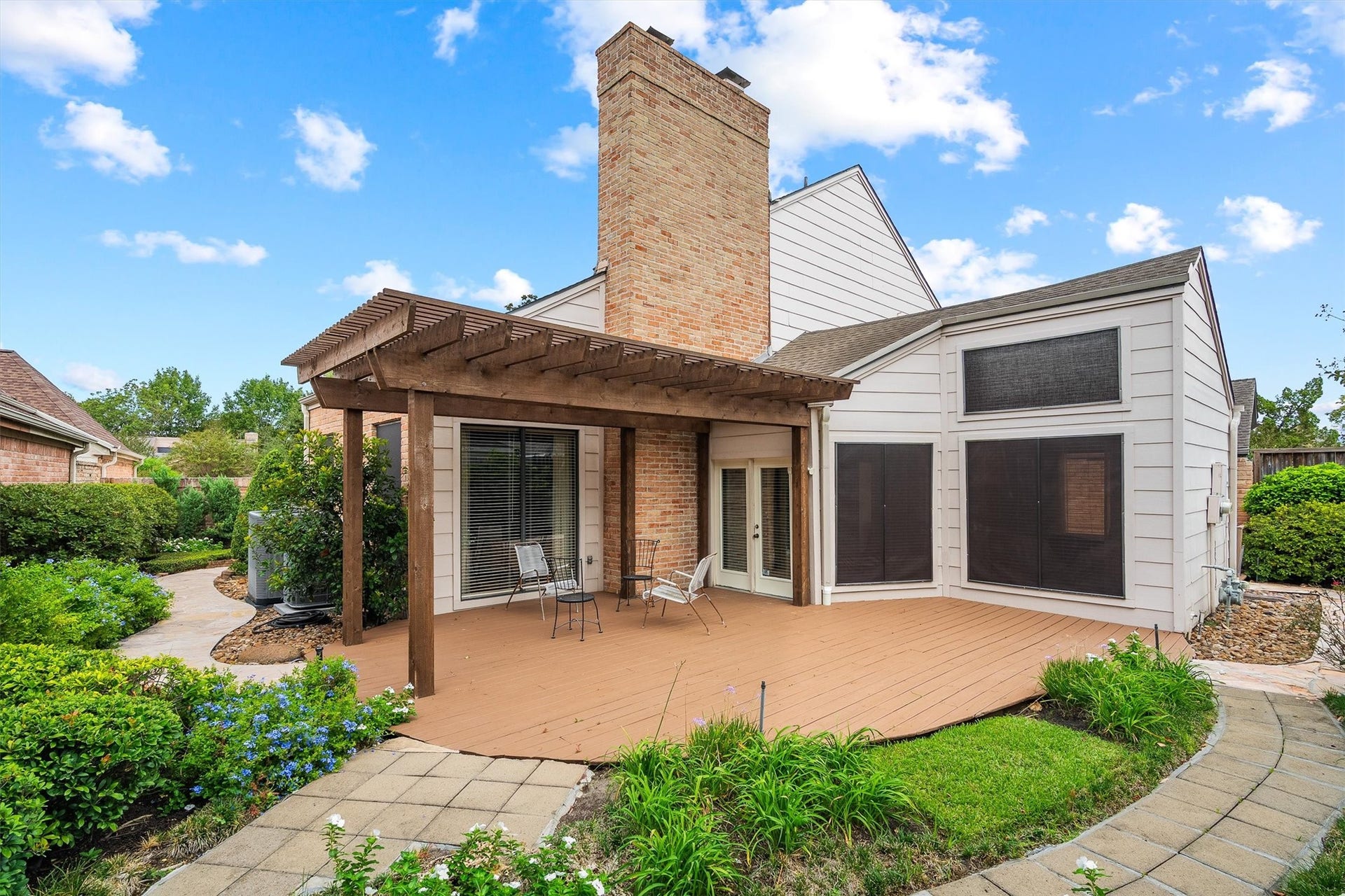 12219 Ravenmoor Drive, Houston, TX 77077 Charming backyard with a spacious wooden deck and pergola, perfect for relaxing or entertaining, surrounded by lush landscaping and garden pathways.