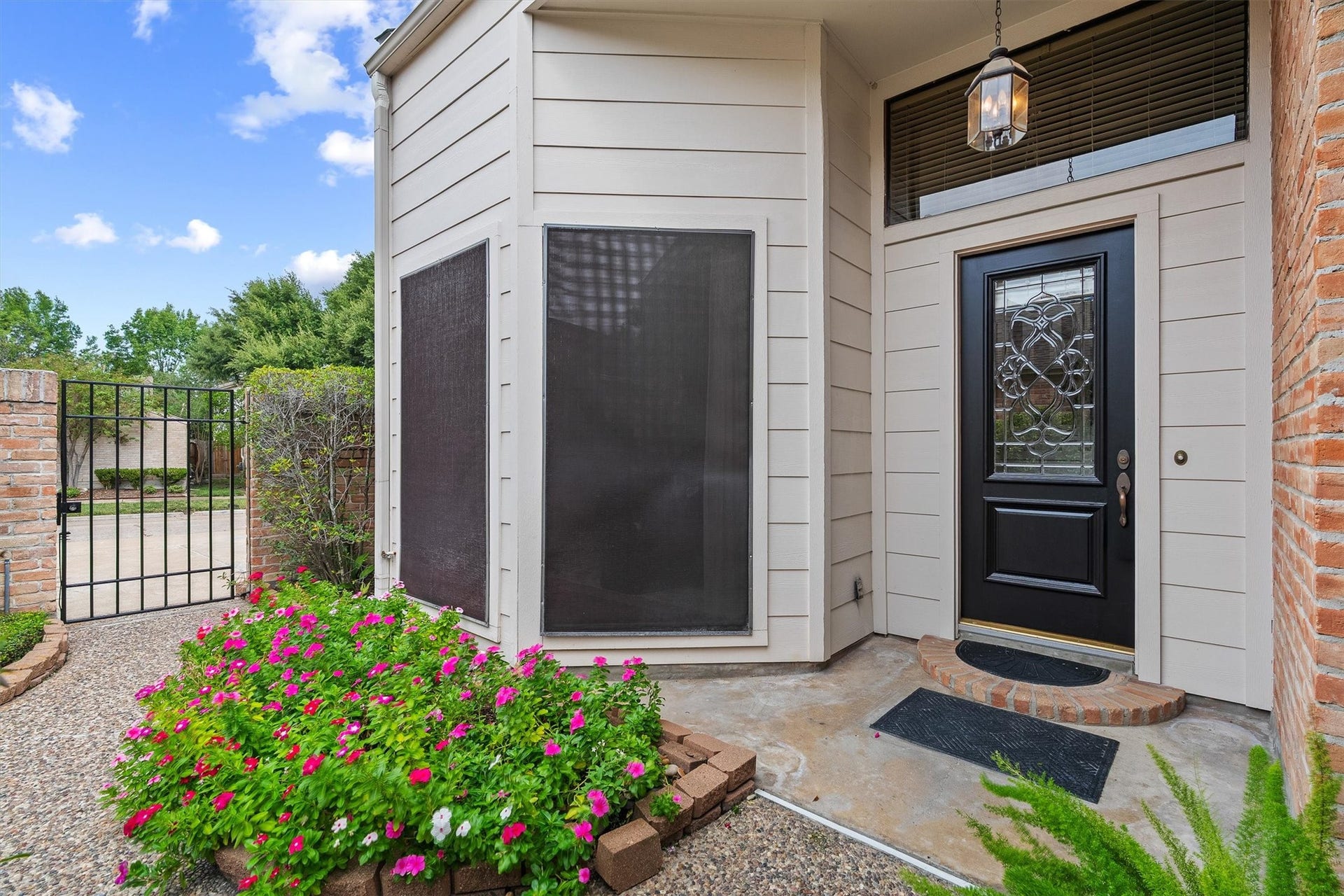 12219 Ravenmoor Drive, Houston, TX 77077 Attractive entrance with elegant black door and intricate glass design, surrounded by lush flowerbeds and a private gated pathway.
